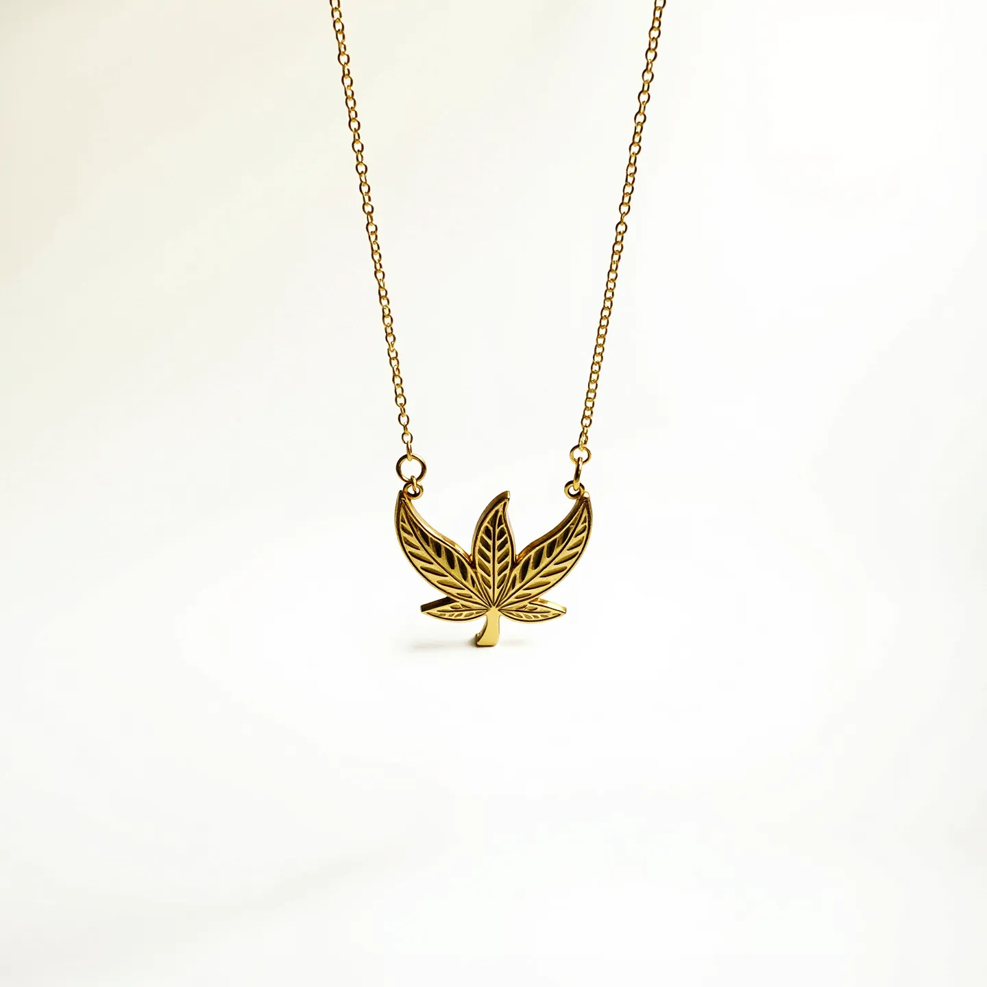 This custom necklace features a delicate gold chain that supports an intricately designed pendant shaped like a stylized leaf. The pendant is crafted in a gold-tone metal, highlighting detailed vein patterns within the leaf structure. The chain is linked directly to the pendant on each side, ensuring the leaf remains centered when worn. The necklace is likely to have a lobster clasp or similar style for secure fastening, though this particular detail is not visible in the image. The minimalist design emphasizes the elegance of the leaf motif, making it a versatile accessory for various outfits.