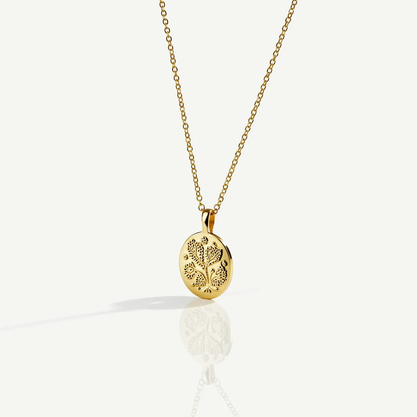 This custom necklace features a delicate gold chain that holds an intricately designed pendant. The pendant is oval-shaped and crafted from polished gold, showcasing an engraved tree motif on its surface. The chain is likely made from a fine quality gold alloy, contributing to its elegant appearance. The pendant is adhered to the chain with a small gold bail, completing the seamless design. The necklace includes a clasp that is most likely designed for ease of use and security, ensuring the pendant is displayed prominently when worn.