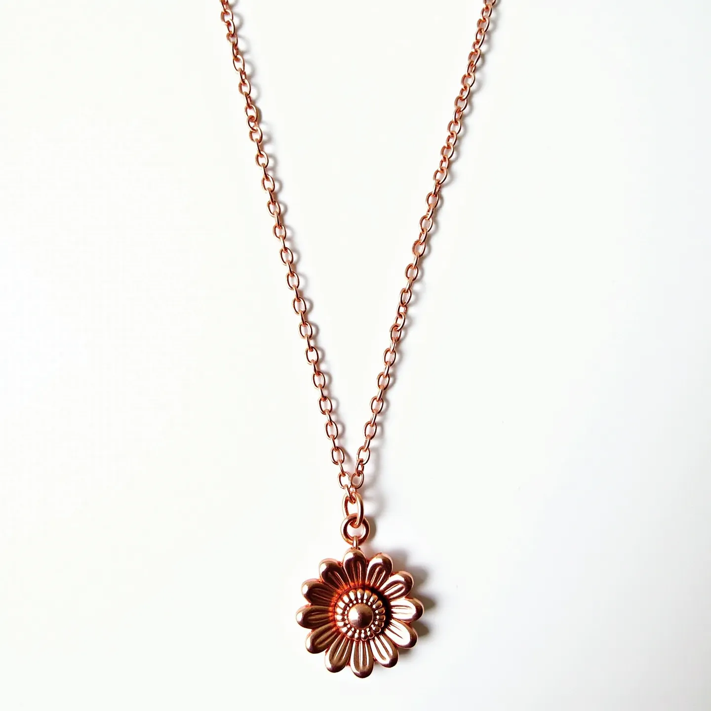 This custom necklace features a delicate chain crafted from a warm-toned metal, likely copper or rose gold. The pendant is designed as a flower with detailed, layered petals and a textured center, mimicking a daisy or sunflower. The metalwork showcases careful craftsmanship with a polished finish. The chain appears to be a simple link style, offering an understated elegance. The clasp type is not visible, but the pendant is securely attached to the chain with a jump ring, allowing for slight movement. Overall, the necklace combines natural inspiration with refined metal artistry for a charming effect.