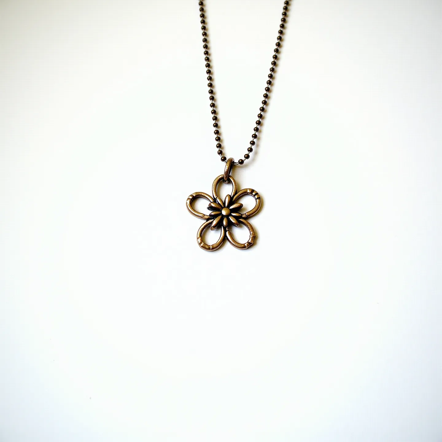 This custom necklace features a delicate floral pendant made from a brass-like metal, showcasing five curved petals with a central, detailed core. The pendant is attached to an antiqued ball chain, which complements the rustic and vintage aesthetic of the piece. The closure mechanism appears to be a standard ball chain connector, ensuring a seamless and secure attachment. The overall design highlights an artisanal approach, emphasizing simplicity and elegance with its choice of materials and openwork floral motif.