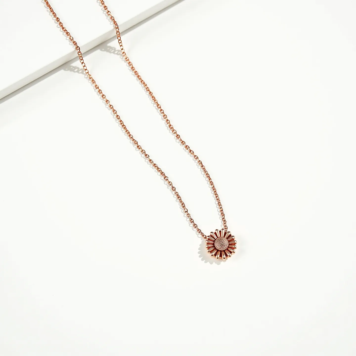 This daisy necklace features a delicate design with a central daisy charm, likely crafted from a rose gold-tone metal. The petals and center of the daisy are intricately fashioned, offering a subtle shine and texture. The necklace is secured with a fine chain that complements the daisy motif, adding elegance and cohesion to the overall look. The necklace appears to have a simple clasp, likely a spring ring or lobster clasp, providing a secure and seamless attachment.