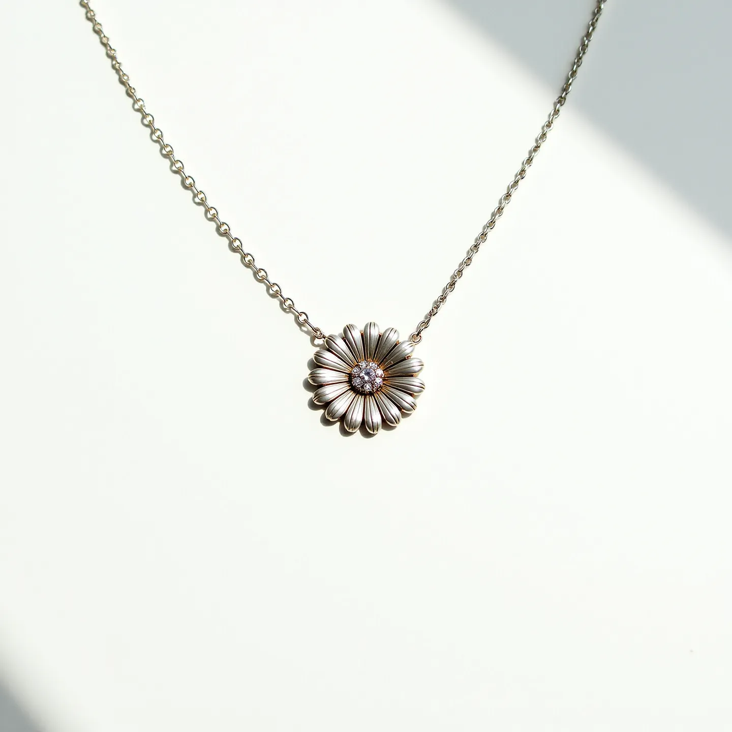 This daisy necklace features a delicate floral pendant crafted with detailed metalwork, likely silver or white gold, forming the petals of the daisy. At the center of the flower, a round cut gem, possibly a diamond or cubic zirconia, is set, adding a touch of sparkle. The gemstone is held securely in place by a simple prong or bezel setting, complementing the overall elegant design. A fine chain is attached to the daisy pendant, integrating seamlessly with the design, and a clasp is likely incorporated to ensure secure wear.