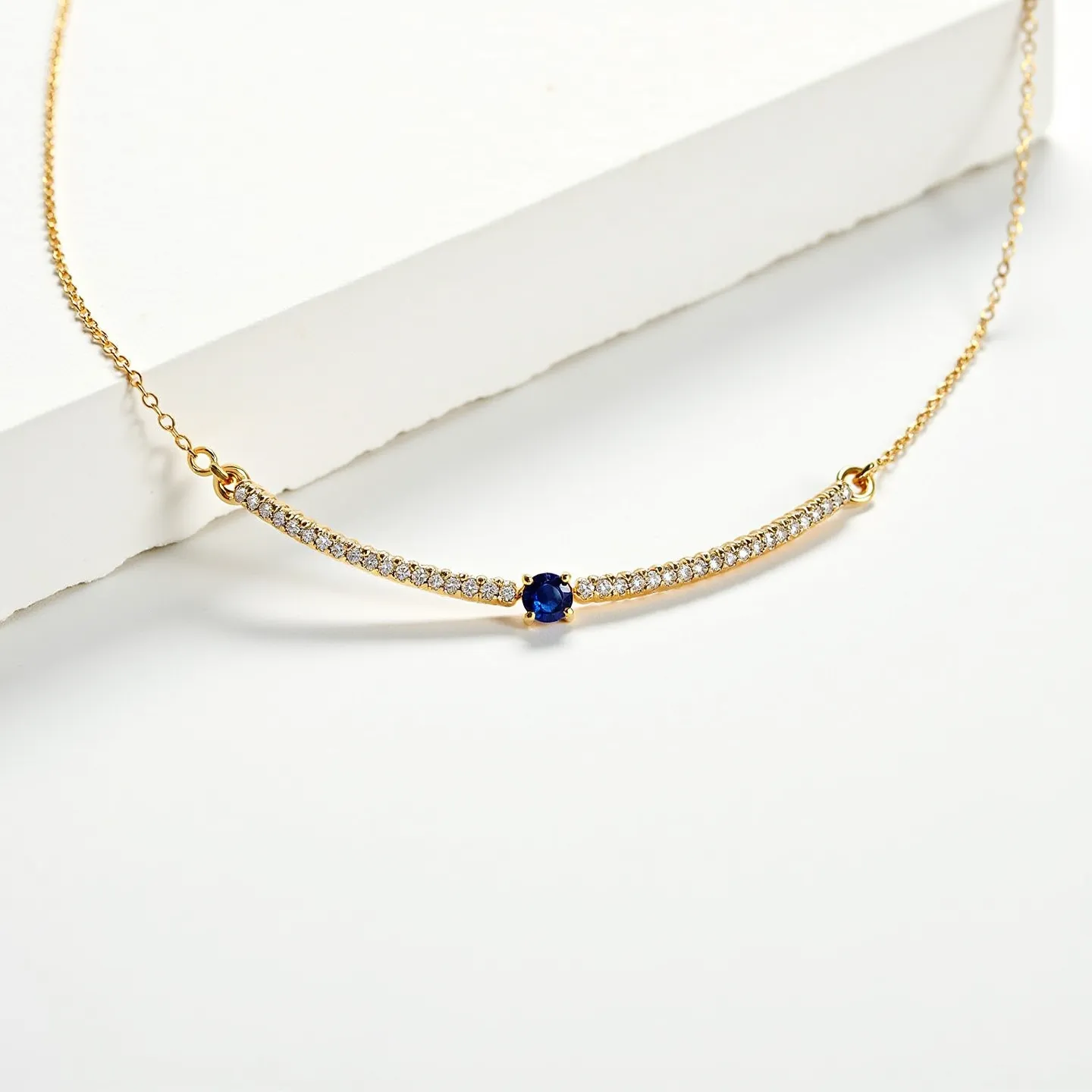 This diamond choker necklace features a delicate gold chain adorned with a curved bar centerpiece. Along the bar, there is a row of small, round-cut diamonds set in a pavé setting, lending a continuous sparkle along its length. At the center of the bar, a single round-cut blue sapphire is prominently set, creating a striking focal point. The necklace is connected by unobtrusive loop attachments, ensuring a seamless and elegant appearance.