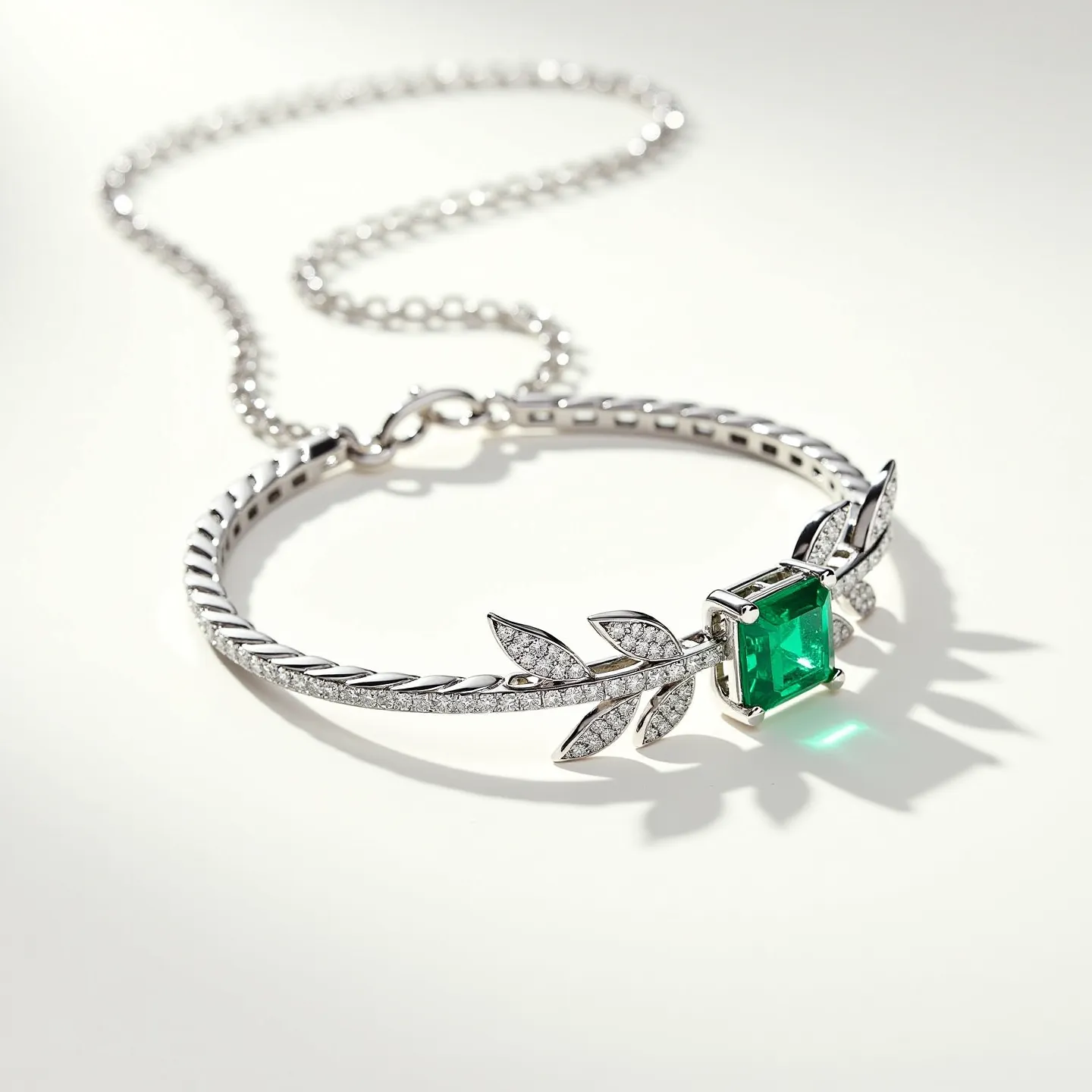 This diamond choker necklace features an exquisite emerald-cut green gemstone prominently set at its center, held securely by a four-prong setting that enhances its brilliance. The necklace is adorned with small, sparkling diamonds in a pave setting, which embellish the leaf-like motifs on either side of the central gem and add a delicate shimmer. The metal appears to be a polished white gold or platinum, offering a sophisticated contrast to the vibrant green stone. The choker transitions into a chain link strap, concluding with a classic clasp for secure attachment.