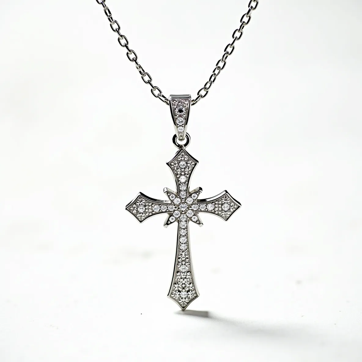 This diamond cross necklace features a beautifully crafted cross pendant encrusted with numerous small, brilliant-cut diamonds, each meticulously set in a pavé style, which gives the piece a uniformly sparkling appearance. The cross itself has gracefully curved edges and a central starburst design accentuated by larger diamonds, adding depth and focus to the pendant. It is made of a lustrous metal, likely white gold or platinum, which enhances the brilliance of the diamonds. The pendant is attached to a sturdy chain by a diamond-studded bail, providing a cohesive and elegant connection. The chain itself appears to be of a cable-link construction, offering durability and complementing the pendant's design.