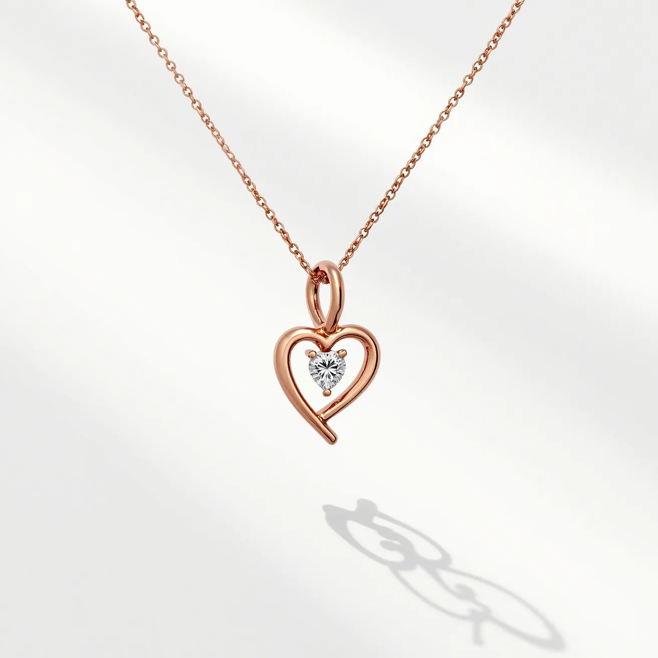 This diamond heart necklace features a delicate pendant crafted from a rose gold material, shaped into an open heart. At the center of the heart, a beautifully cut round diamond is securely set in a classic prong setting, allowing the gemstone to sparkle with brilliance. The pendant is elegantly suspended from a fine, matching rose gold chain, which contributes to the necklace's sophisticated and cohesive design. The necklace is equipped with a simple yet secure clasp, ensuring ease of wear and durability.