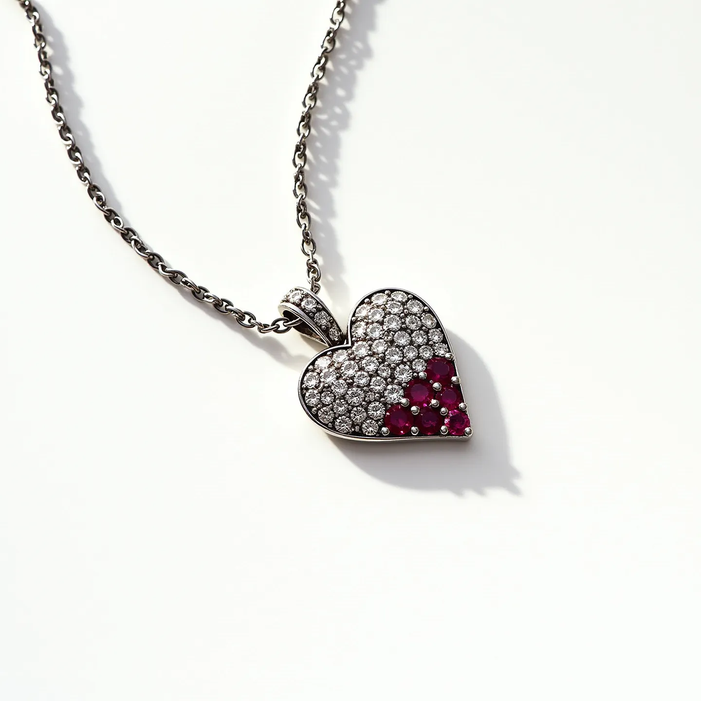 This diamond heart necklace features a delicate heart-shaped pendant adorned with an array of sparkling gemstones. The upper part of the heart is encrusted with brilliant-cut diamonds, providing a shimmering surface that catches the light beautifully. The lower portion is embellished with vivid red gems, likely rubies, adding a striking contrast to the design. These stones are meticulously set in a pavé setting, enhancing their brilliance and offering a seamless surface. The pendant is attached to a polished metal chain, which could be crafted from white gold or platinum, contributing to the piece's elegant and luxurious appeal. The chain is linked with a sturdy clasp, ensuring both security and ease of wear.