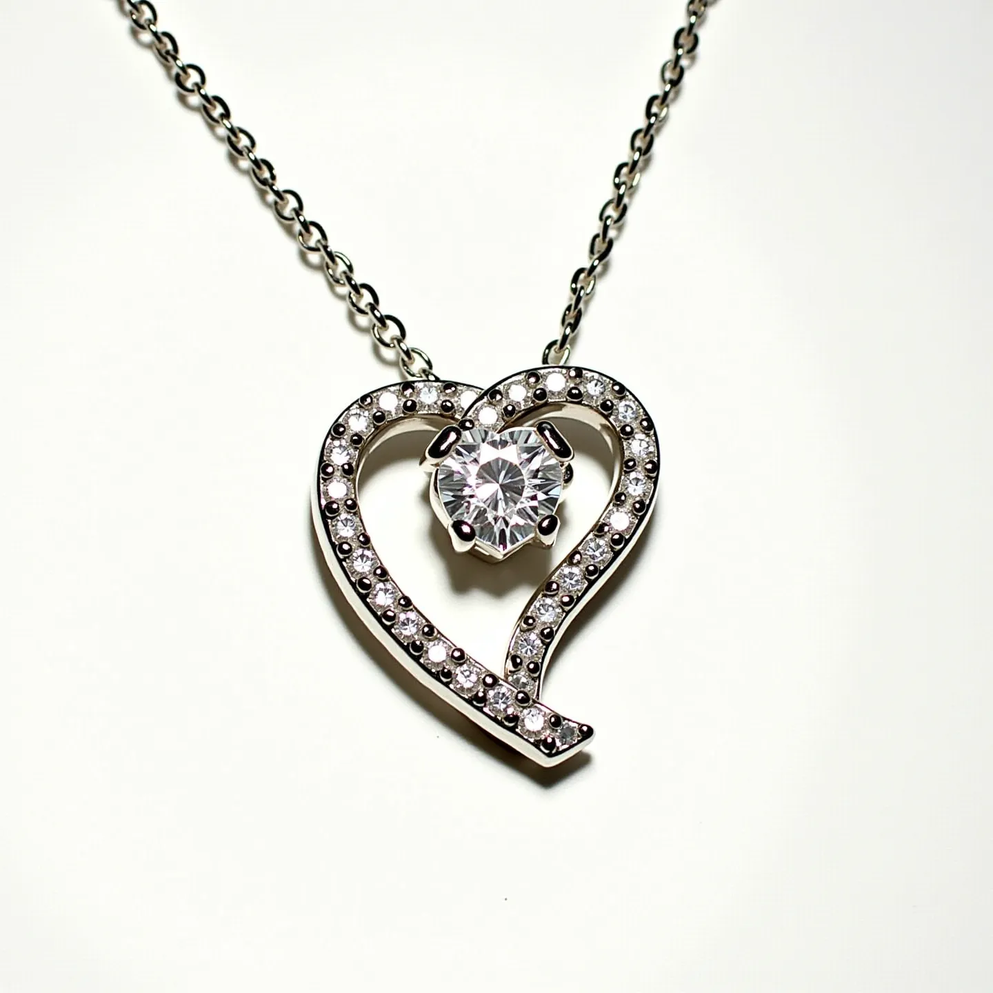 This diamond heart necklace features a delicate heart-shaped pendant adorned with a series of small, round diamonds set into the silver or white gold frame, providing a glittering border. At the center of the heart, a larger round-cut diamond is prominently displayed in a prong setting, allowing it to catch light from various angles for added brilliance. The pendant is securely attached to a fine chain, which is likely made of matching metal to ensure a cohesive and elegant look. A classic spring ring or lobster clasp may be present to fasten the necklace, ensuring ease of wear and a secure fit.