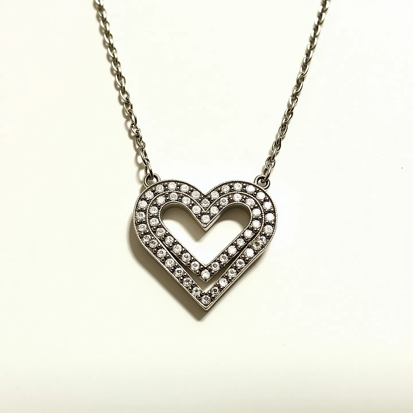 This diamond heart necklace features a heart-shaped pendant encrusted with a series of small, round-cut diamonds. The stones are meticulously set in a pave style, providing a shimmering effect across the pendant. The metal appears to be a polished white gold or platinum, adding a sleek and luxurious appeal to the overall design. The necklace is attached to a delicate, yet sturdy chain that complements the pendant, using small loops to connect seamlessly. The clasp is not visible, but likely uses a common and reliable mechanism for such jewelry, ensuring both security and ease of use.