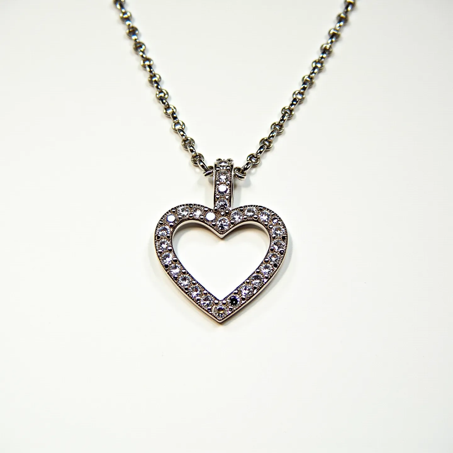 This diamond heart necklace features a delicate heart-shaped pendant adorned with small, round diamonds set in a pavé style, providing a shimmering effect. The pendant is likely crafted from a shiny, silvery metal, such as white gold or platinum, which enhances the brilliance of the diamonds. The necklace is secured to a chain with a simple loop, ensuring it hangs elegantly. The chain itself appears to be made of the same metal as the pendant, with interlocking links providing a classic and timeless look.