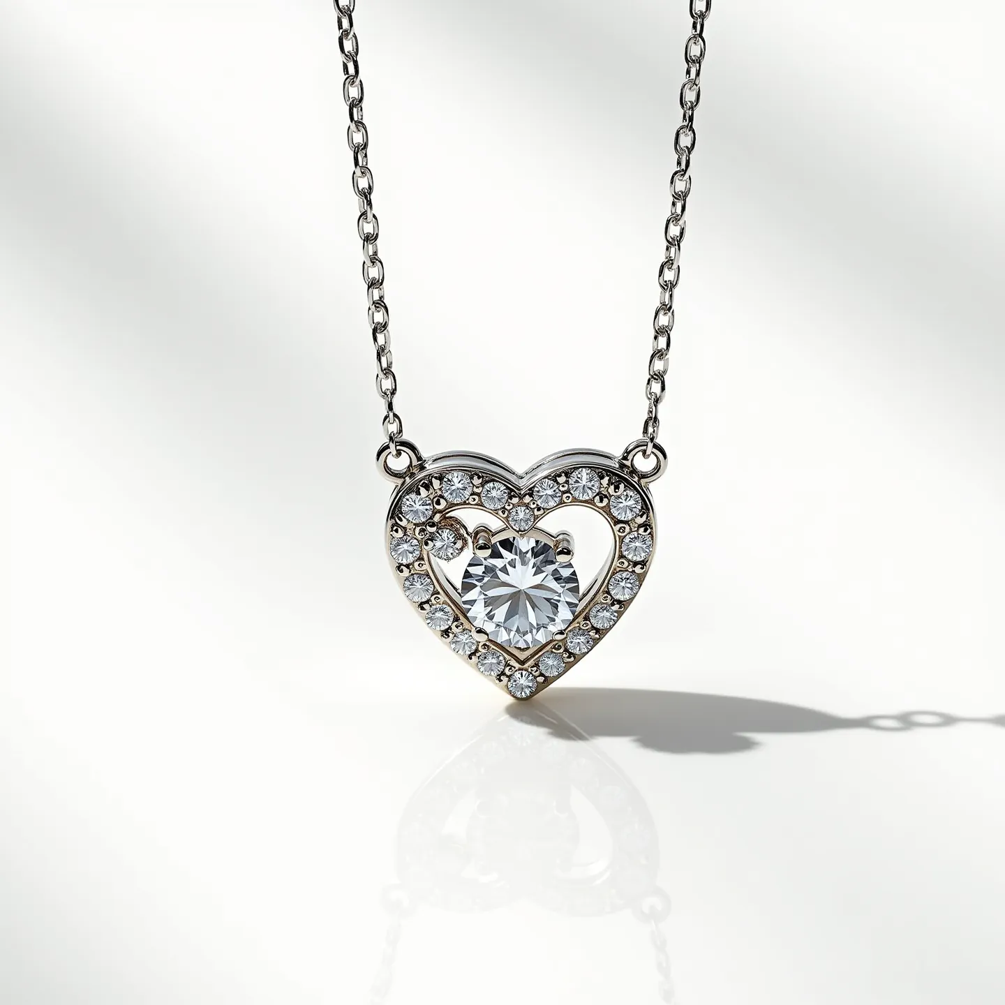 This diamond heart necklace showcases a delicate heart-shaped pendant encrusted with small, round-cut diamonds in a pavé setting that elegantly outlines the heart. The centerpiece of the necklace is a larger, round brilliant-cut diamond, securely held in a prong setting at the center of the open heart design, adding significant sparkle and elegance. Crafted from a lustrous metal, likely white gold or platinum, it enhances the brilliance of the diamonds. The heart pendant is suspended from a dainty chain, connected via small loops on either side of the heart, which are integrated into the design for a seamless appearance. The clasp or attachment mechanism is not visible in the image.