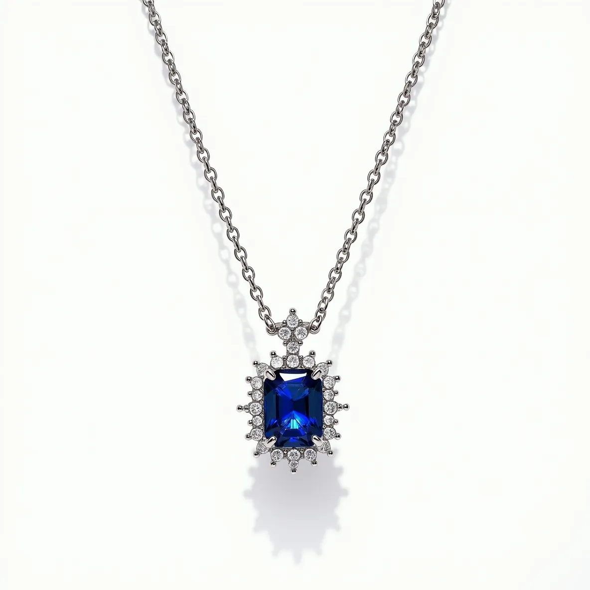 This diamond necklace features a striking design centered around a large, square-cut blue sapphire set in a prong setting. Surrounding the sapphire are multiple round, brilliant-cut diamonds, enhancing the pendant’s elegance with their sparkling brilliance. The diamonds are securely set in metal prongs, creating a halo effect that adds depth to the piece. The necklace is suspended on a delicate metal chain that complements the pendant's sophisticated style. It is likely that the chain and setting are made of a high-quality metal such as white gold or platinum, adding to the necklace's luxurious appeal. The necklace is completed with a traditional clasp, ensuring a secure and comfortable fit for the wearer.