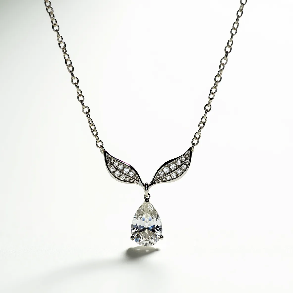 This diamond necklace features a delicate chain crafted from a sleek metal, possibly white gold or platinum, which supports an elegant pendant design. The central focal point is a sizable pear-cut diamond, expertly mounted in a three-prong setting that maximizes its brilliance and showcases its clarity. Above the main stone, two symmetrical, leaf-shaped components are adorned with small round diamonds in a pavé setting, enhancing the necklace's sparkle and adding intricate detail. The attachment and clasp are seamlessly integrated into the design, providing a secure and sophisticated closure mechanism that complements the overall aesthetic.