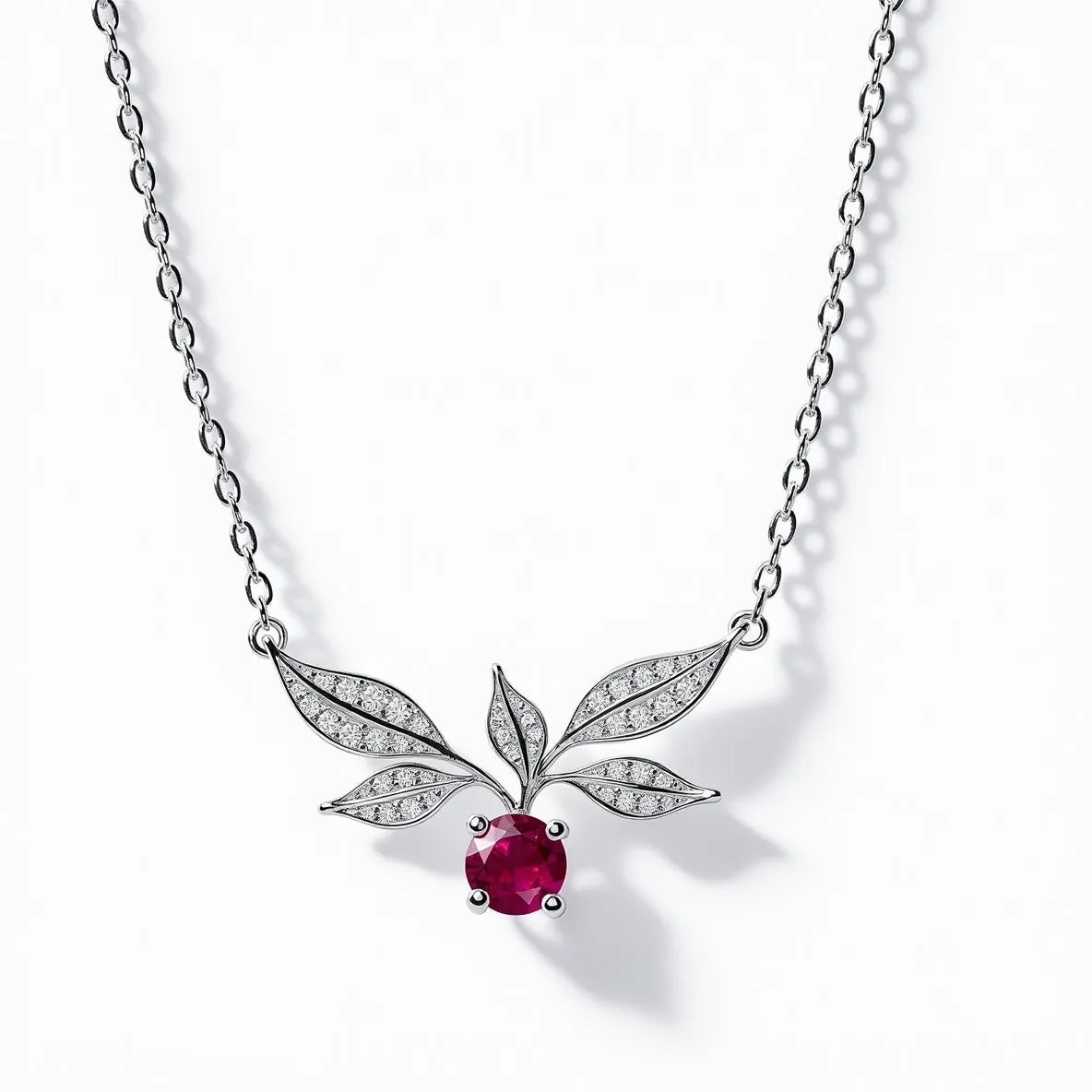 This diamond necklace features a delicate chain in a polished metal, likely white gold or platinum. At its center is a striking design of intertwined leaves, each set with small, round-cut diamonds that add a sparkling elegance to the piece. The focal point is a deep red, round-cut gemstone, possibly a ruby, held securely by a prong setting that enhances its vibrant color. The necklace is completed with a classic lobster clasp, ensuring both security and ease of wear. The craftsmanship of the necklace highlights the harmonious blend of the materials and gemstones, creating a timeless and elegant accessory.