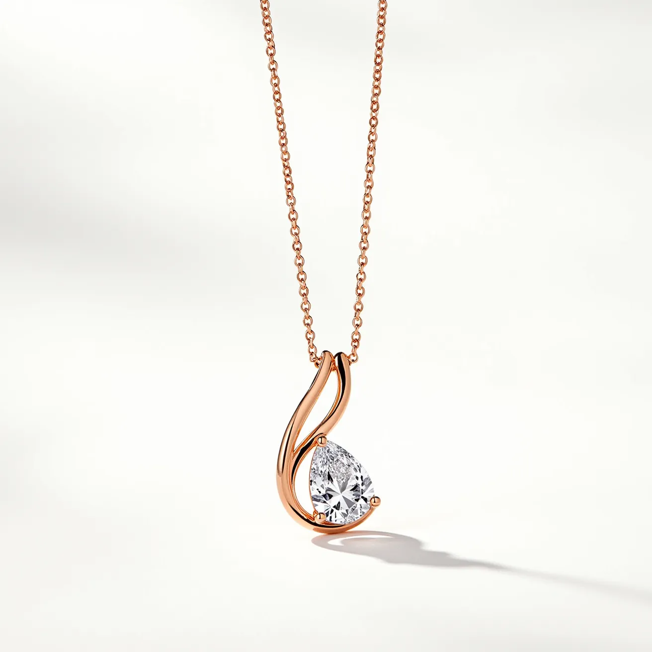 This diamond necklace features a delicate chain crafted from rose gold, complementing the pendant's elegant design. The necklace showcases a pear-shaped diamond, expertly cut to enhance its brilliance and sparkle. The diamond is securely held in a three-prong setting, which is beautifully integrated into the fluid lines of the pendant, suggesting a contemporary and graceful aesthetic. The attachment appears to be a simple yet sturdy clasp that ensures secure wear. The combination of materials and design elements results in a timeless piece that marries modern elegance with classic luxury.