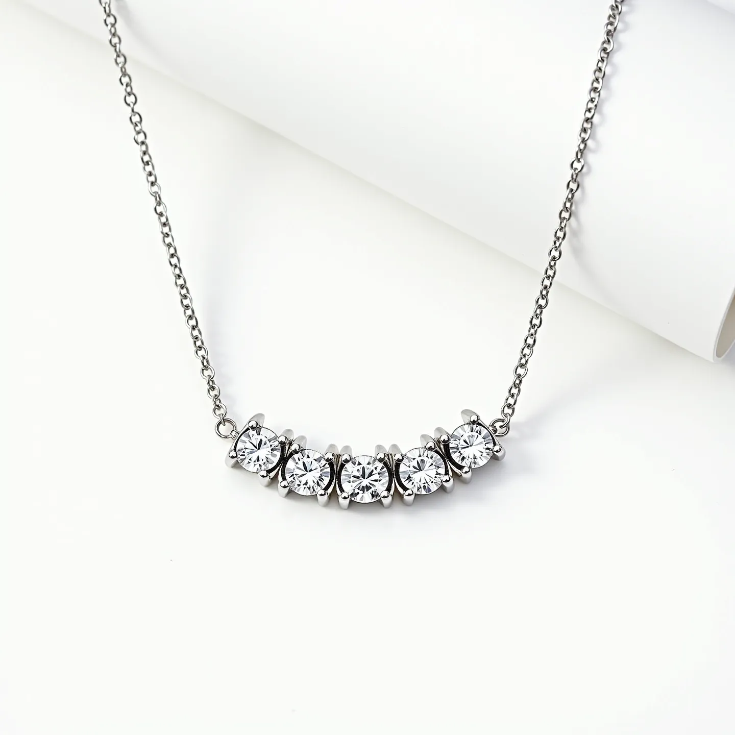 This diamond tennis necklace displays a delicate arrangement of five round-cut diamonds set in a sleek, polished metal that appears to be white gold or platinum. The diamonds are precisely aligned in a bezel setting, creating a seamless and elegant look. The necklace features a fine chain, complementing the brilliance of the diamonds while ensuring comfortable wear. The attachment is likely a secure clasp, designed to uphold both functionality and style in this sophisticated piece of jewelry.