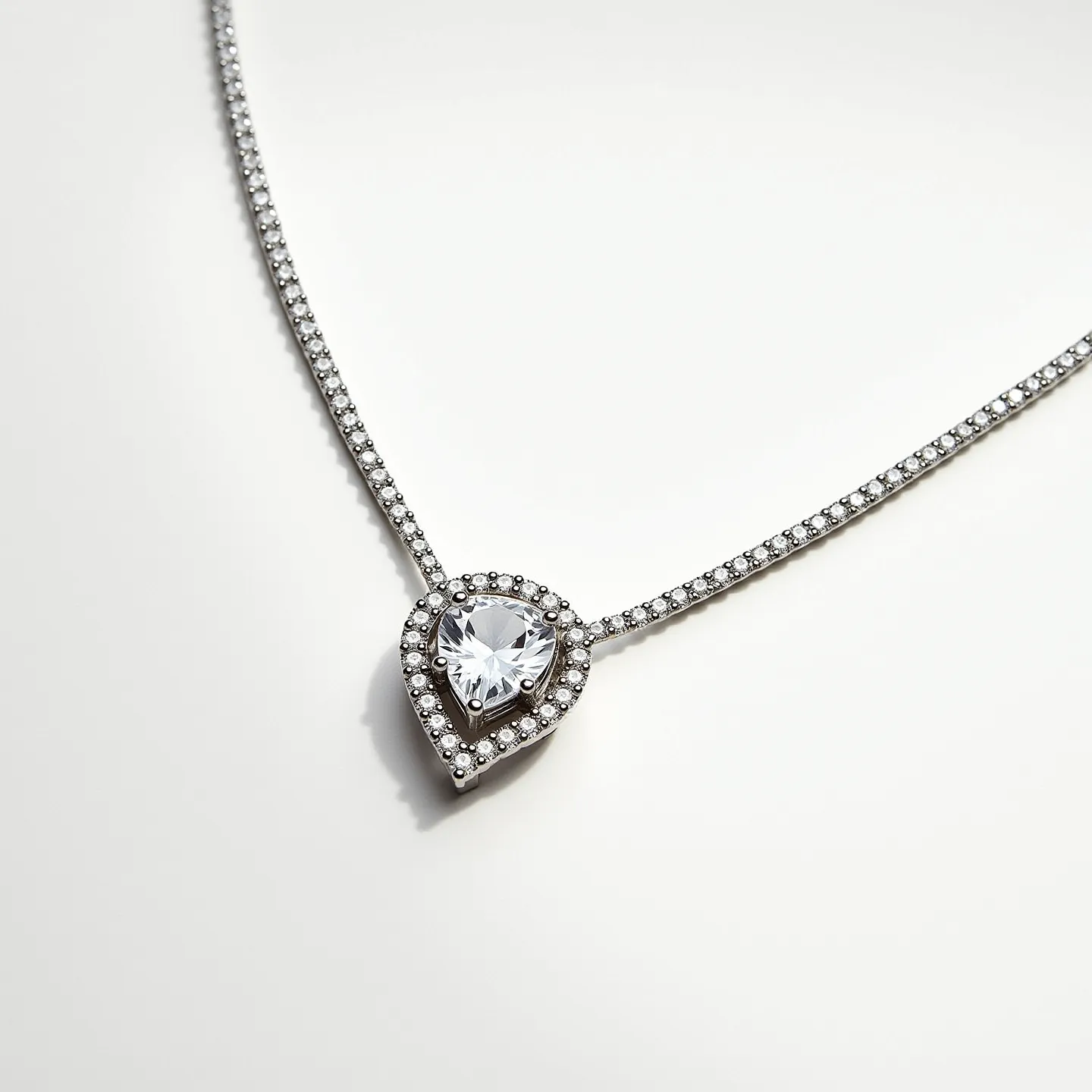 This diamond tennis necklace features a series of small diamonds set in a classic and elegant line, each stone held securely in a prong setting. The necklace is crafted from a white metal, likely white gold or platinum, complementing the sparkle of the diamonds. A stunning focal point is a pear-shaped diamond, expertly cut to enhance its brilliance, and surrounded by a halo of smaller round diamonds in a pavé setting. The necklace is secured with a discreet clasp that maintains the fluidity and continuity of the design.