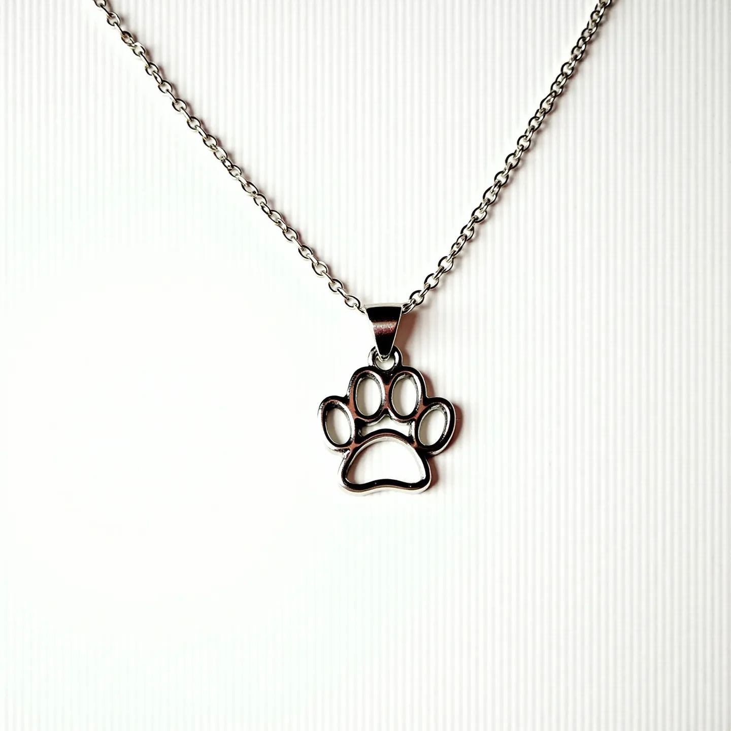 This dog necklace features a delicate chain made from what appears to be silver or stainless steel, known for its durability and sleek finish. The pendant is an intricately designed paw print charm that hangs gracefully from the chain. The paw print has a smooth, polished surface that complements the overall metallic look of the piece. The necklace is secured with a standard lobster clasp, offering ease of wear and secure fastening. Its minimalist yet charming design makes it suitable for casual wear and dog lovers alike.