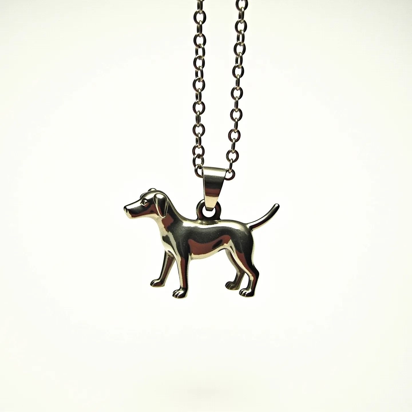 This dog necklace features a sleek metallic pendant shaped like a dog, showcasing smooth lines and a polished finish. The pendant is likely made of stainless steel, given its shiny, reflective surface and durability. It hangs from a chain with interlocking oval links, each with a uniform size and a matching metallic finish. The clasp is not visible in this view, but the overall design suggests a simple and functional attachment to complement the minimalist aesthetic of the piece. No gems or stones are present, emphasizing the clean, modern look of the necklace.