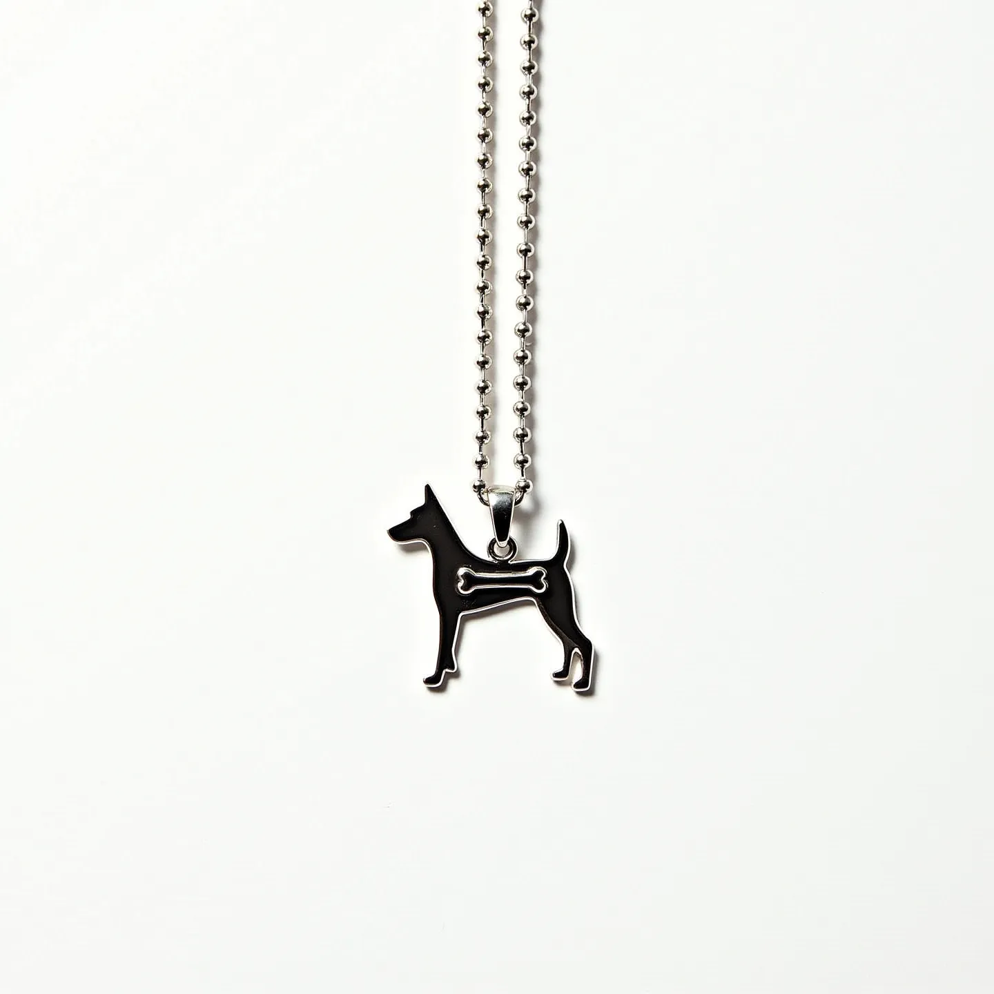 This dog necklace features a distinctive silhouette of a dog with a bone detail within the body. The pendant appears to be crafted from a metal with a sleek, polished finish, giving it a modern and stylish look. The necklace is attached to a beaded chain, likely made of a similar metal, with rounded beads forming the links. The pendant is connected to the chain through a loop, secured by a simple clasp, providing ease of wear while maintaining the overall aesthetic. The design is minimalist yet striking, offering a playful nod to the canine theme.