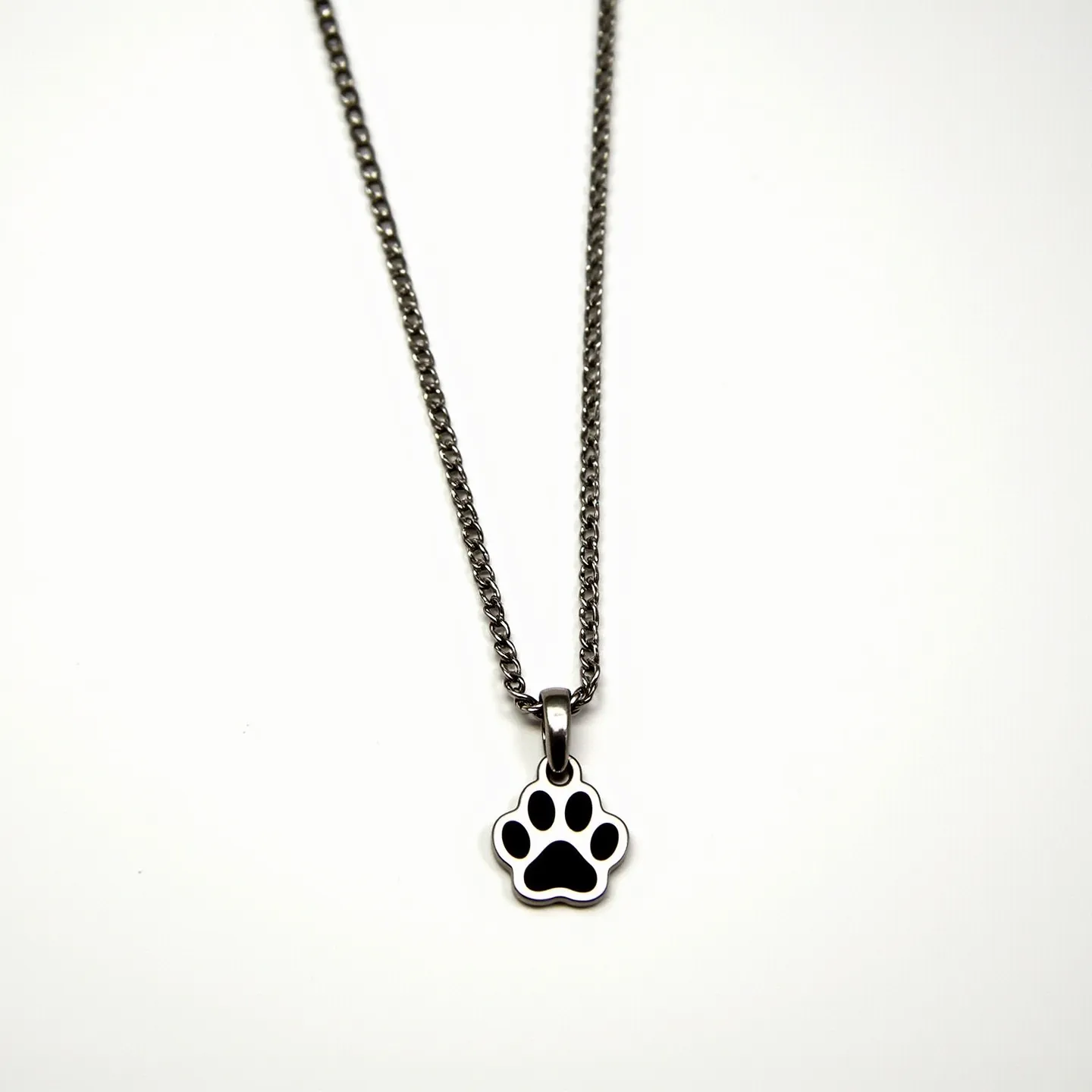 This dog necklace features a sleek metal chain with a polished finish, likely stainless steel, providing durability and a modern aesthetic. The pendant is shaped like a dog's paw, crafted from a similar metal with a smooth, reflective surface. The paw design includes a black enamel inlay, adding contrast and visual interest. The pendant is attached to the chain via a simple metal bail that allows it to move freely along the chain. The necklace closes with a standard lobster clasp, ensuring a secure and adjustable fit. This accessory combines minimalistic elegance with a charming, pet-themed design.