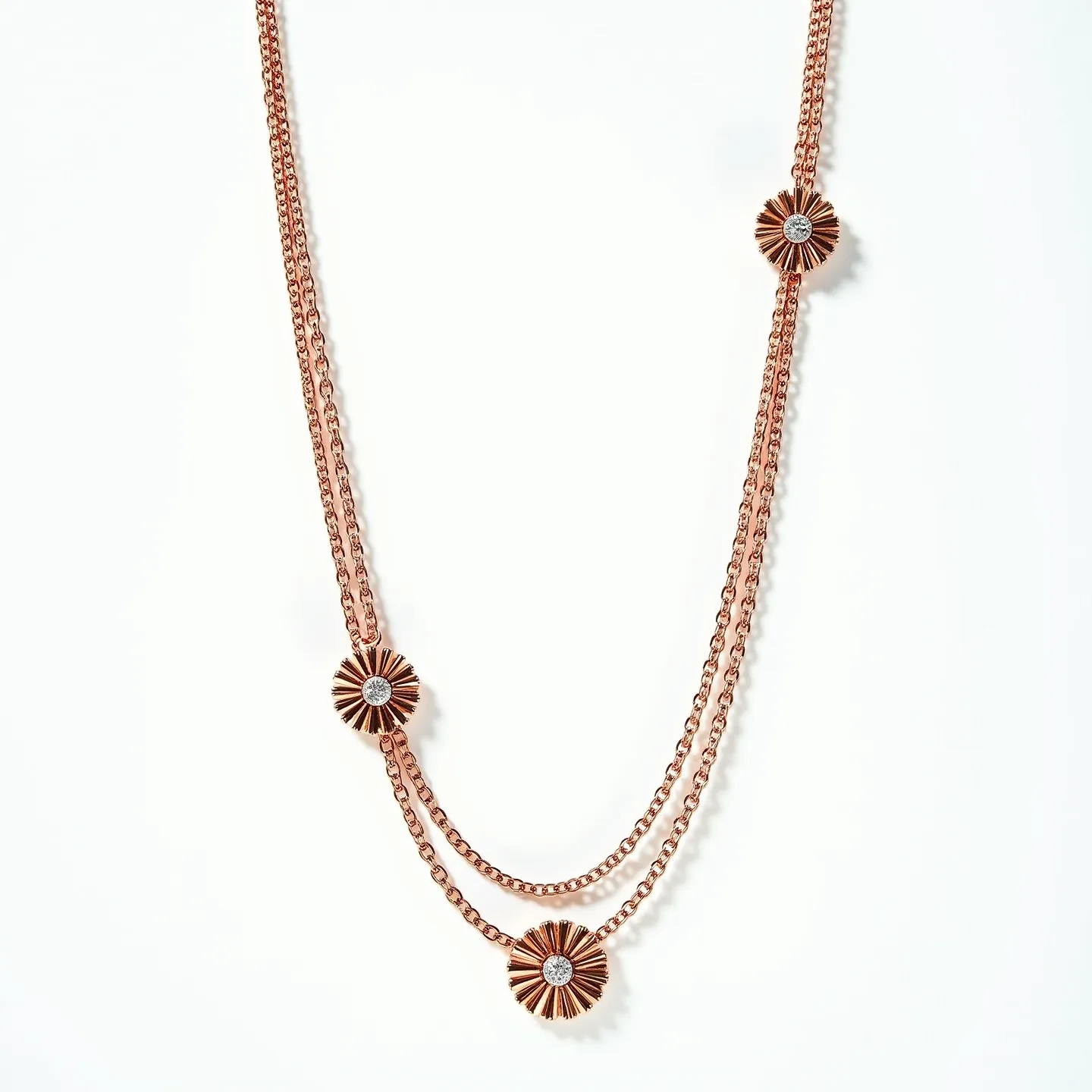 This double necklace features two linked chains crafted from a material resembling rose gold, giving it a warm, elegant appearance. The design includes three circular floral motifs spaced along the chains, each adorned with a central gem. These gems appear to be round-cut and are set in the middle of the flower-like designs, highlighting their brilliance. The motifs have a sunburst pattern, enhancing the overall aesthetic with a touch of sophistication. The necklace likely has a delicate clasp or hook at the back, ensuring a secure fit when worn.