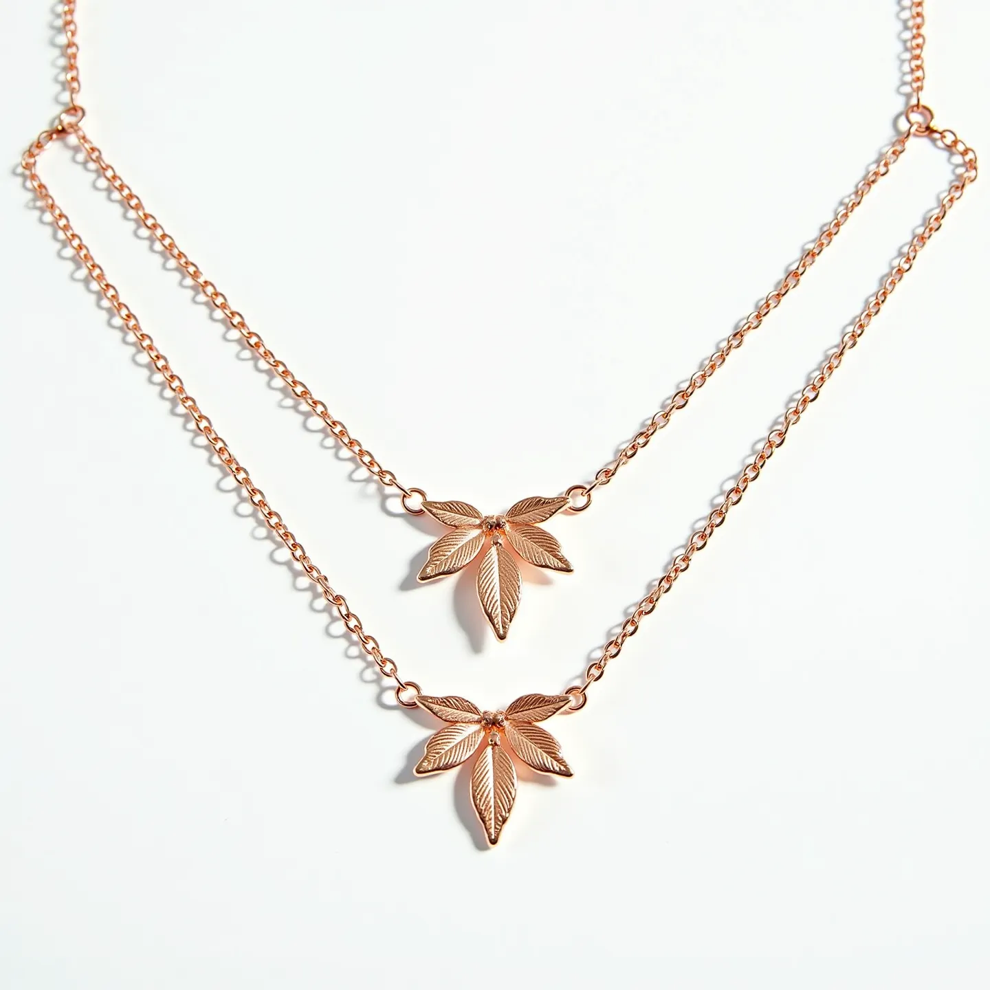 This double necklace features delicate gold-toned chains, each holding a detailed leaf pendant at the center. The pendants are crafted with intricate detailing, showcasing a textured leaf design that emanates elegance and natural charm. The chains appear to be thin and elegantly linked, adding to the overall light and understated look of the piece. The necklace is likely to be fastened with a simple clasp mechanism, maintaining a cohesive and refined appearance.