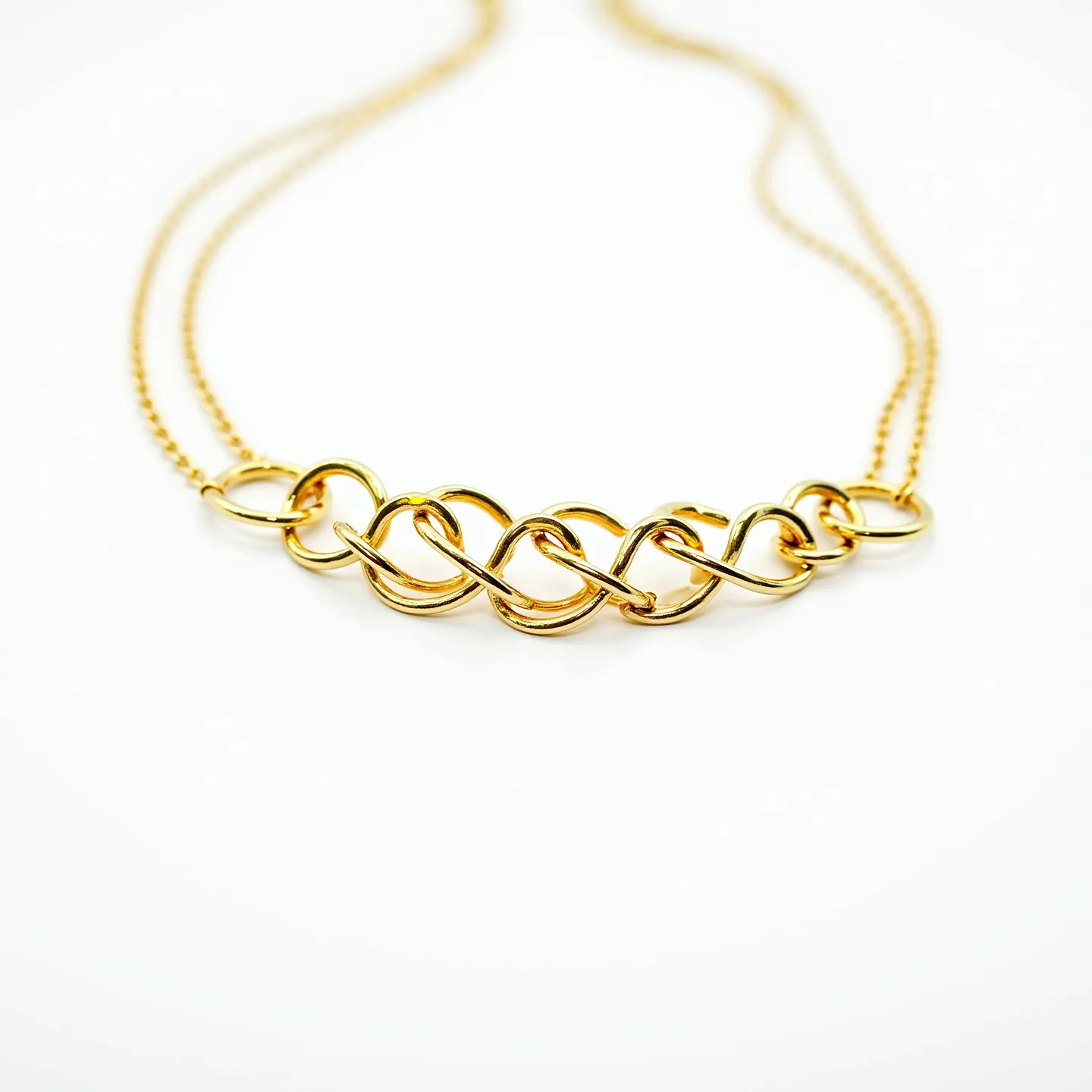 This double necklace features a pair of delicate gold chains that are united by a series of intricately linked gold loops, forming an elegant centerpiece. The loops are intertwined in a symmetrical pattern, adding a touch of sophistication and fluidity to the design. The gold material provides a warm, lustrous appearance, enhancing its visual appeal. The necklace is completed with a simple clasp for secure fastening, maintaining both functionality and style. The absence of gemstones keeps the focus on the refined craftsmanship and the graceful interlocking design.