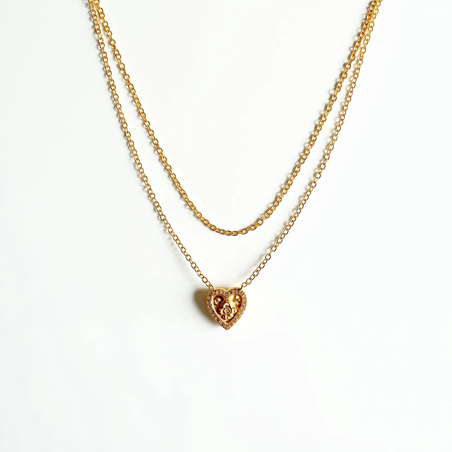 This double necklace features two delicate gold chains, one slightly shorter than the other, creating a layered look. The focal point of the necklace is a heart-shaped pendant that hangs from the longer chain. Embedded within the heart pendant are small, round gems in a classic bezel setting, possibly imitating a diamond or crystal appearance, which add a subtle sparkle to the piece. The pendant itself is detailed with ornate metalwork, enhancing its elegance. The necklace likely secures with a standard spring-ring or lobster clasp, ensuring functionality and ease of wear.