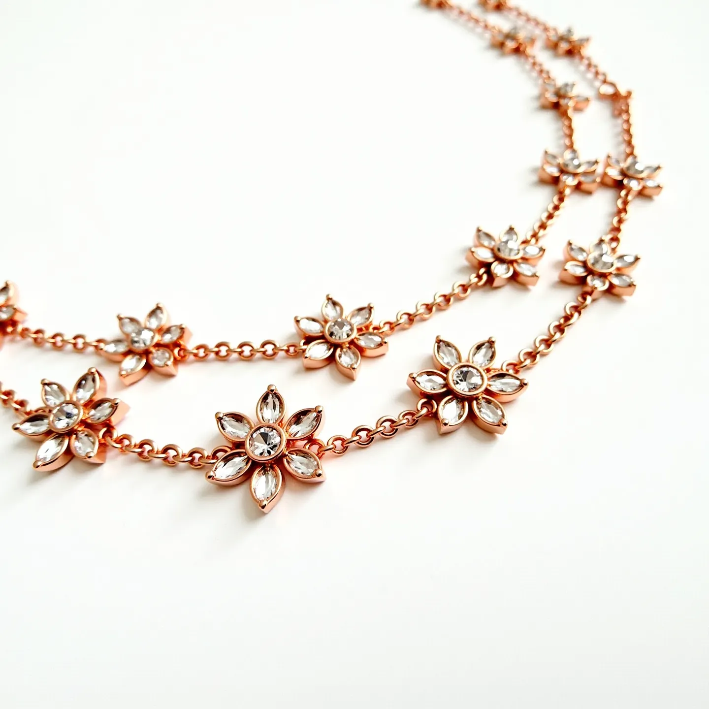 This double necklace features a series of floral designs crafted from a gold-colored metal, creating a warm, luxurious appearance. Each flower consists of a central round stone, likely a clear crystal or diamond simulant, surrounded by marquise-cut stones arranged as petals, all set in a prong setting. The chain links connecting the flowers correspond with the metal's color, seamlessly tying the design together. While the fastening mechanism isn't visible, the chain's delicate yet sturdy construction suggests a refined finish, enhancing the necklace's overall elegance.