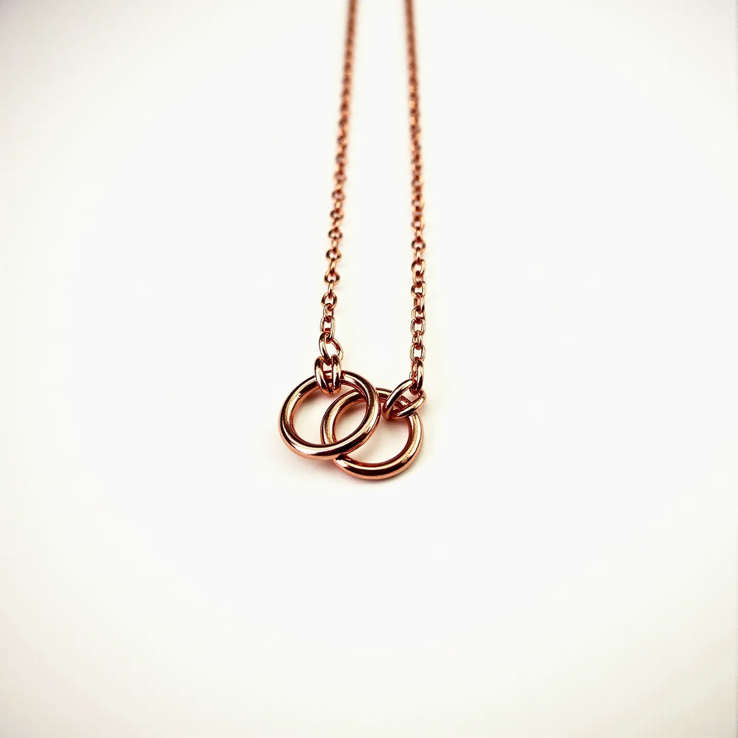 This double necklace features a delicate chain crafted from rose gold metal, giving it a warm, lustrous finish. It includes two interlocking rings, which serve as the primary decorative elements, further emphasizing the necklace's minimalist elegance. The design does not include additional gemstones or embellishments, focusing purely on the geometric interplay of the gold rings. The chains appear to be finely linked, enhancing the fluidity and flexibility of the piece. This necklace likely incorporates a standard clasp to ensure secure wearing while maintaining its sleek aesthetic.