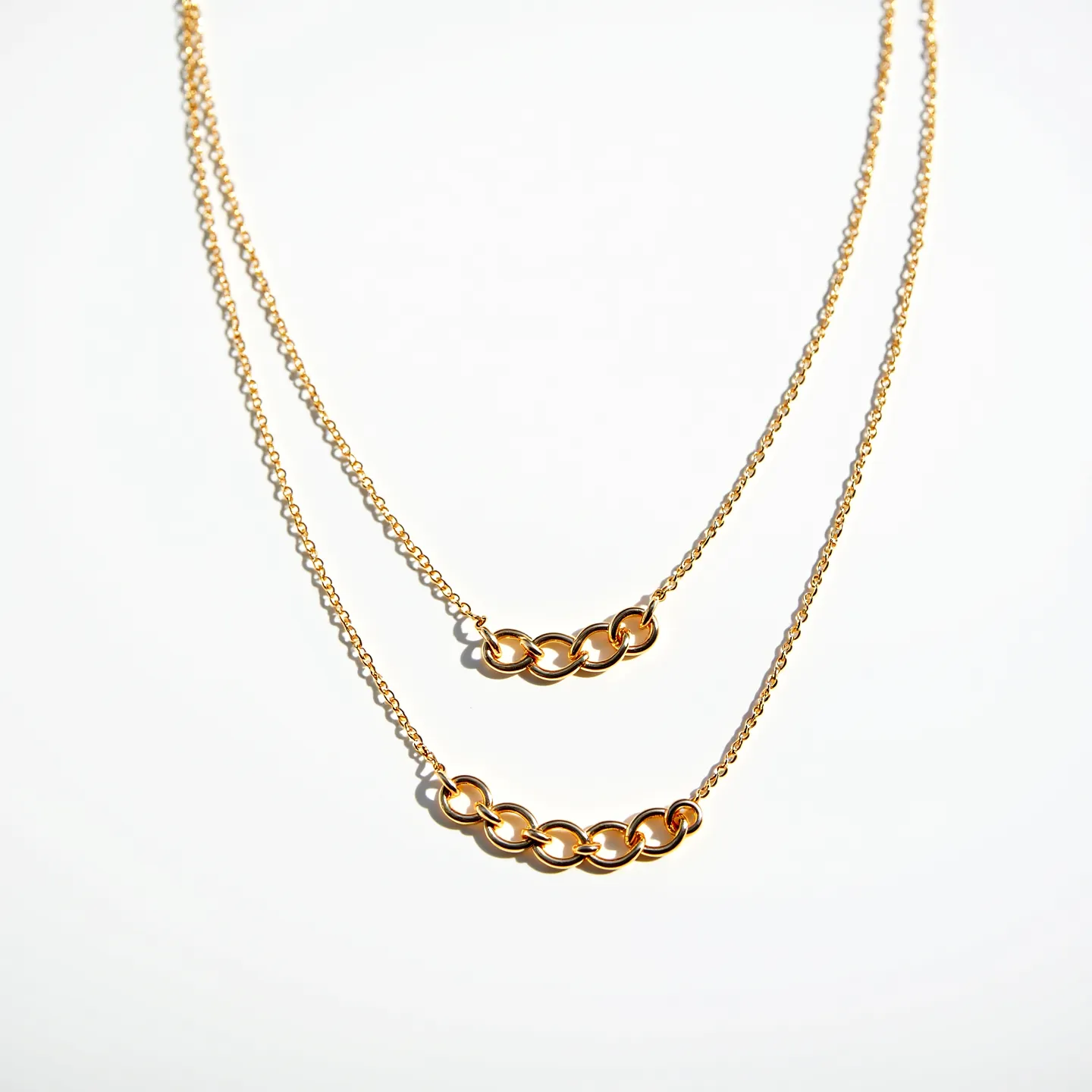 This double necklace features two delicate gold chains of varying lengths, creating a layered effect. Both chains are adorned with a central arrangement of interlocking gold loops, adding an elegant focal point to the piece. The gold loops are smooth and polished, enhancing their reflective quality. The necklace likely closes with a simple lobster clasp or spring ring, ensuring a secure fit while maintaining the minimalistic design. This piece combines simplicity with a touch of sophistication, making it versatile for various occasions.