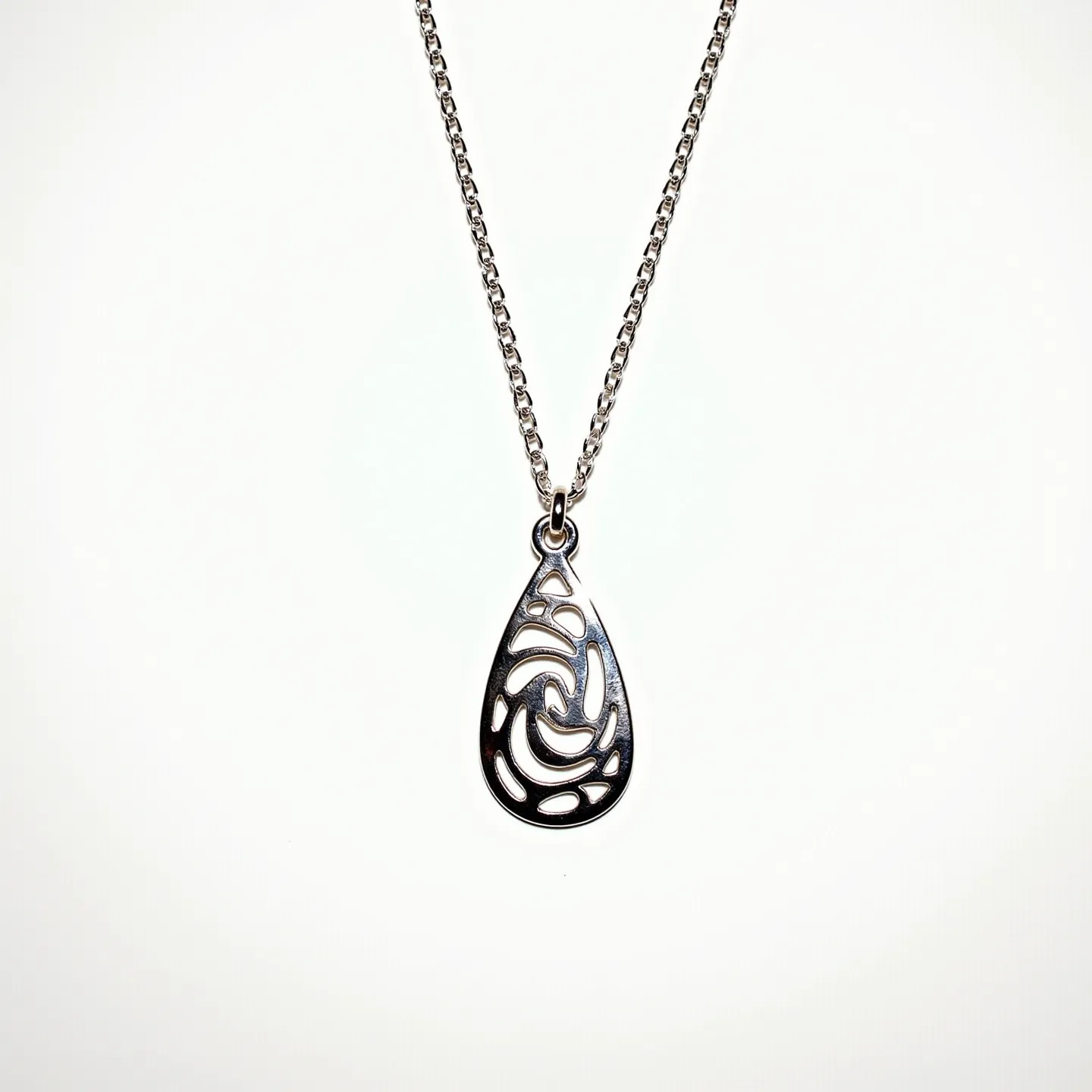 This drop necklace features a delicate chain likely made of silver or a similar metal, from which hangs a teardrop-shaped pendant. The pendant showcases an intricate swirling filigree design, adding a touch of elegance and intricacy to the piece. The metal appears polished, giving it a subtle shine. The pendant is secured to the chain with a simple jump ring, allowing for smooth movement. The chain closes with a clasp, standard for necklaces, providing both security and ease of wear.