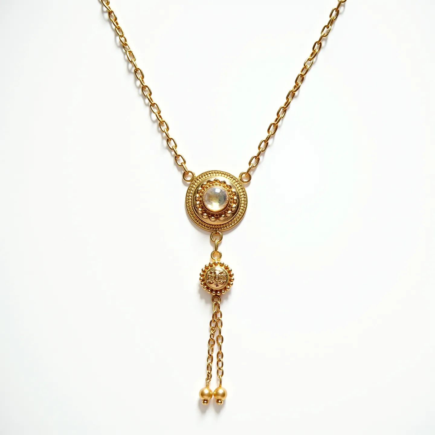 This drop necklace features a gold-toned chain with a central ornamental piece showcasing an intricate design. The focal point is a circular, clear gemstone set into a detailed gold base, likely a cabochon cut, which gives the piece its central shimmer. Below this, a smaller, ornate gold bead is suspended, leading to two delicate chains that drop down, each ending in a small gold sphere. The necklace exhibits a harmonious blend of texture and shine, emphasizing its elegant and ornamental character. The attachment appears to be a classic, easy-to-use clasp, complementing the necklace's refined style.