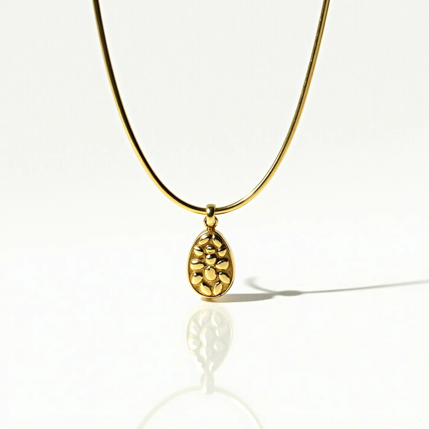 This drop necklace features a sleek, elegant design with a smooth, golden chain. At its center is a distinctive drop-shaped pendant crafted from polished gold. The pendant showcases a unique embossed pattern, adding a touch of texture and depth. It is smoothly attached to the chain with a small, matching gold loop, ensuring a seamless and cohesive look. The necklace exudes sophistication and style, making it a versatile accessory for various occasions.