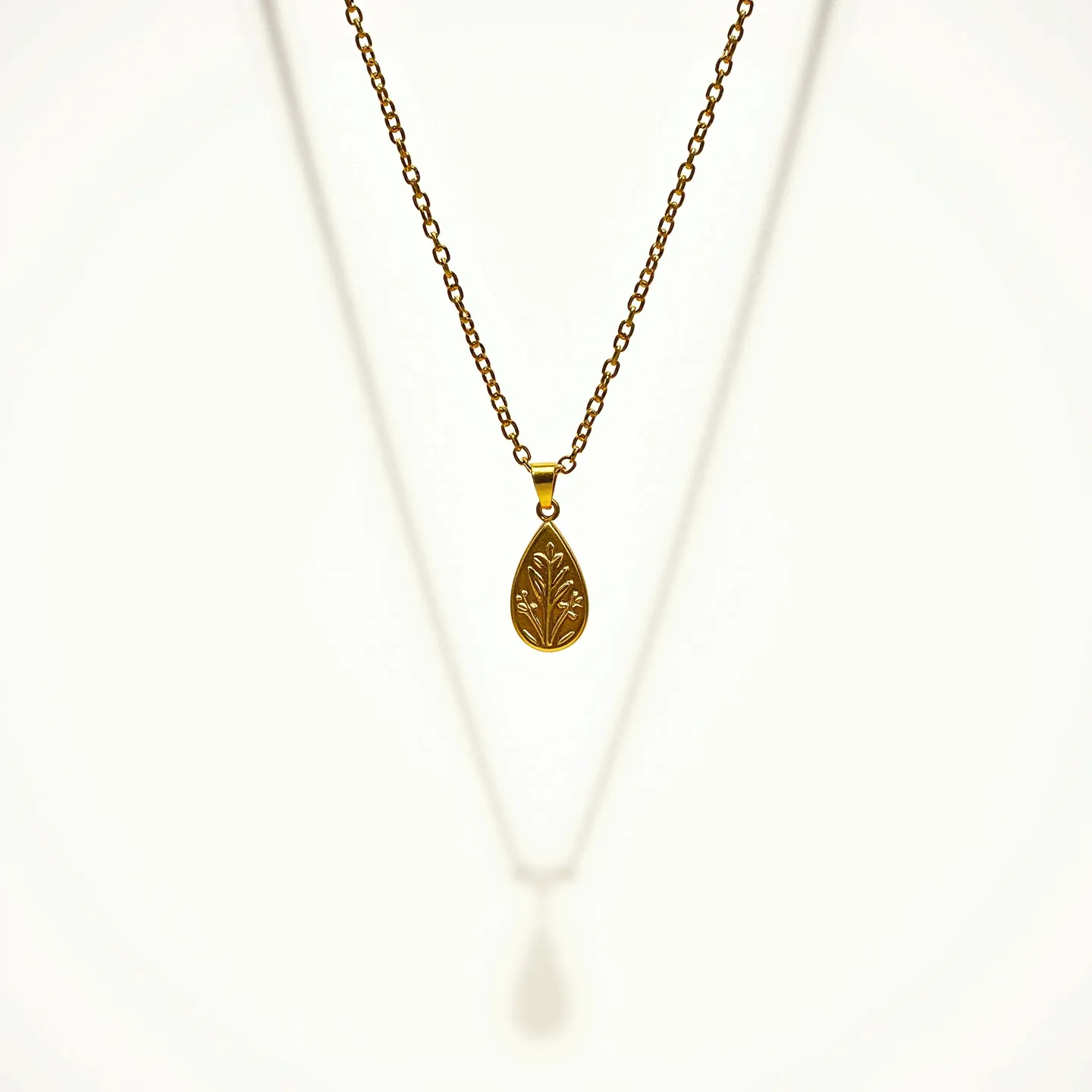 This drop necklace features a delicate chain crafted from a metal with a warm, golden hue. The pendant, also gold-toned, is teardrop-shaped and intricately engraved with a botanical motif, adding an elegant touch to the overall design. The pendant is securely attached to the chain via a small, matching bail. The necklace is finished with a simple, small clasp that seamlessly complements the design, ensuring both a secure fit and ease of wear.