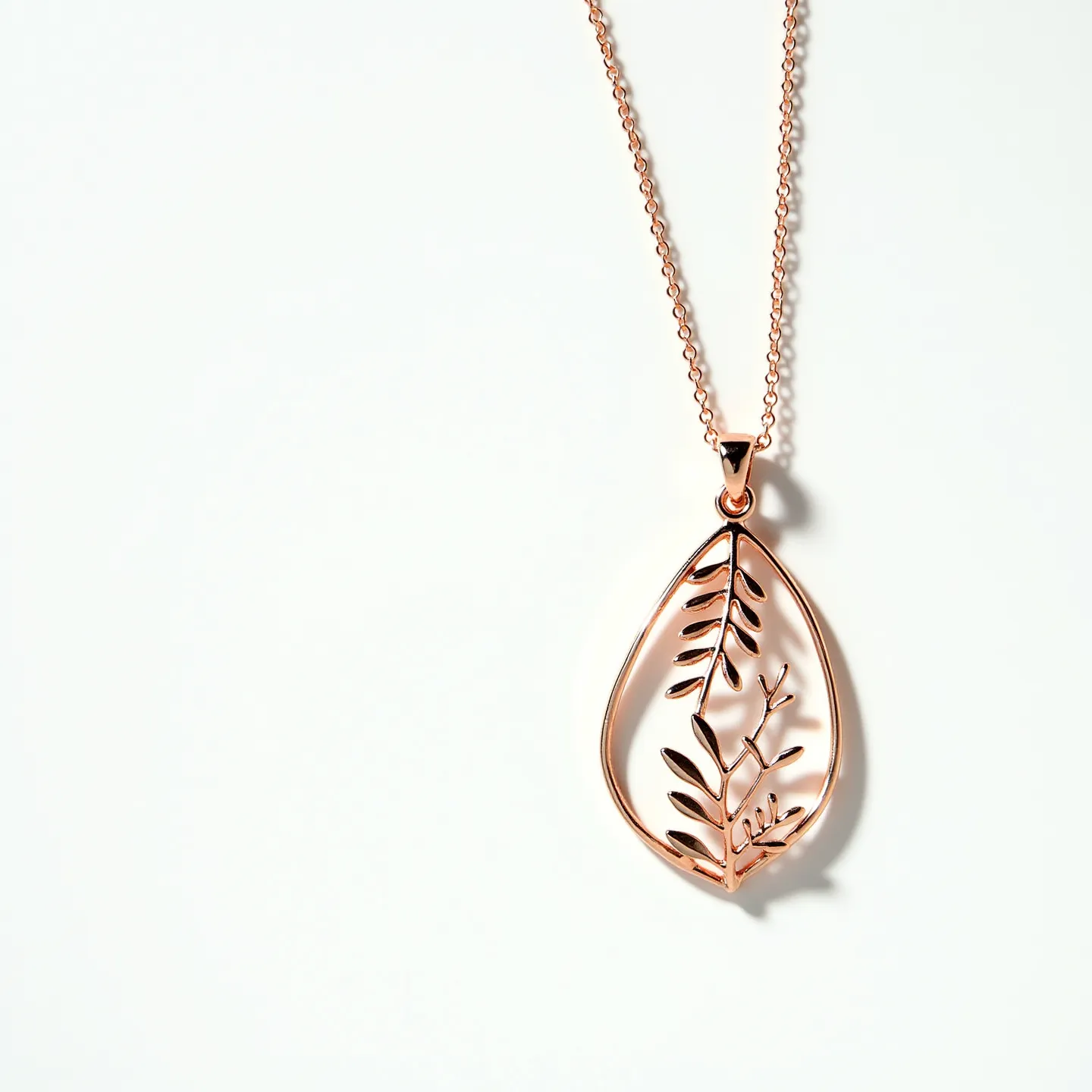 This drop necklace features a delicate rose gold-toned chain paired with an intricately designed pendant in the shape of a leaf. The pendant showcases a cut-out pattern of leaves and branches, adding a touch of elegance and nature-inspired beauty to the piece. The pendant is seamlessly attached to the chain via a small, unobtrusive bail. The necklace likely utilizes a standard lobster clasp for secure fastening, aligning with its refined and contemporary style. This piece, with its minimalist and natural design theme, would serve as a versatile accessory suitable for various occasions.