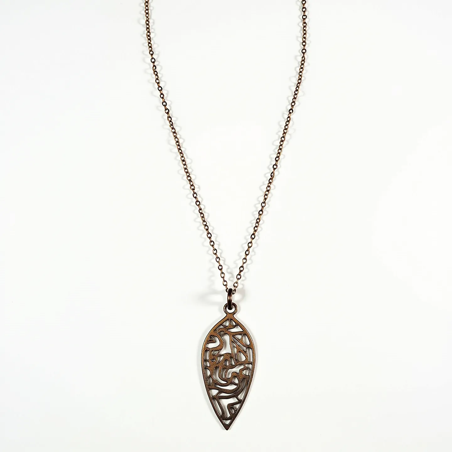 This drop necklace features a delicate chain and a prominent pendant shaped in a pointed drop design. The pendant exhibits an intricate cut-out pattern with swirling lines, giving it an artistic and openwork appearance. It appears to be made of a metal with a warm, bronze-like finish. The chain is composed of interlinked circles, suggesting a simple and classic cable chain style. The pendant is attached to the chain via a small loop at the top. The necklace likely fastens with a standard clasp mechanism at the back, completing its elegant and timeless design.