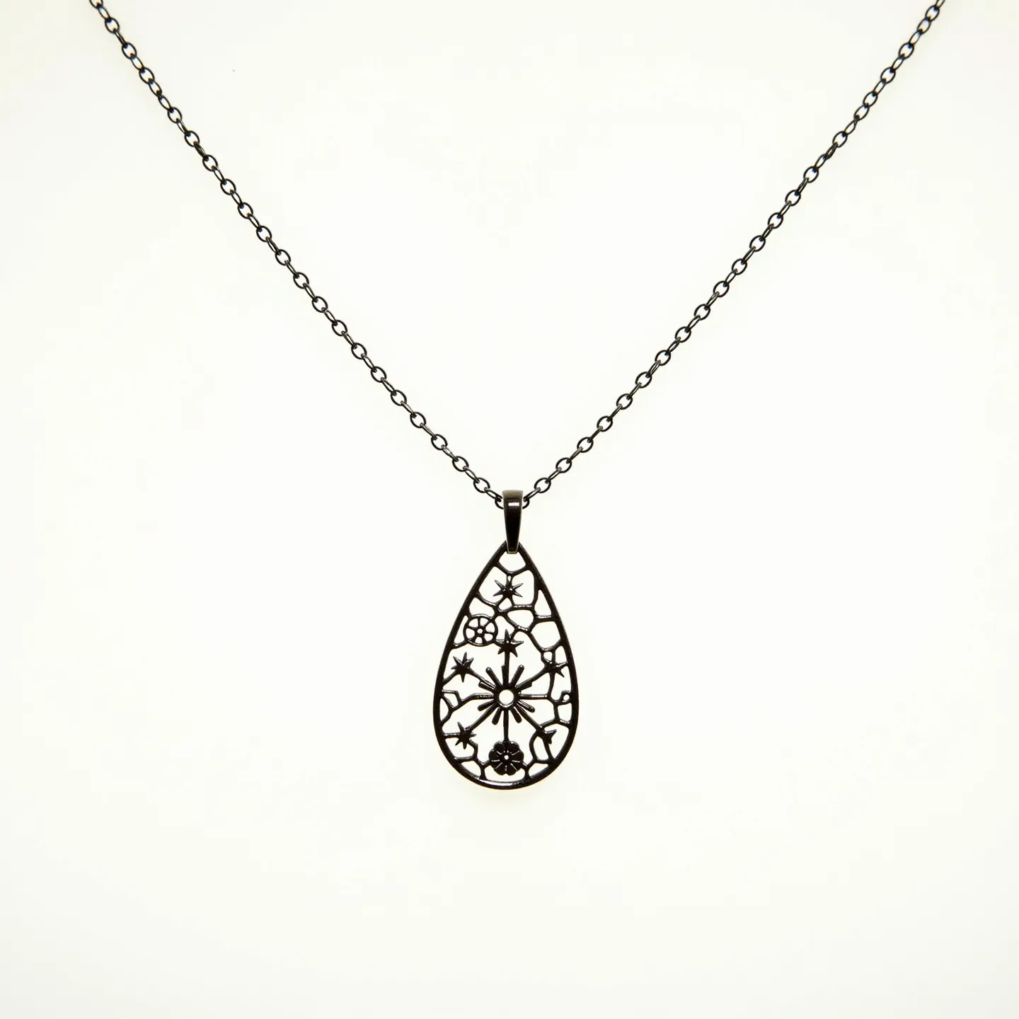 This drop necklace features an intricately designed pendant made from a dark metal, showcasing a delicate lace-like pattern with floral motifs. The pendant is suspended from a fine chain with uniformly sized links, which appears to be crafted from the same dark metal, creating a cohesive look. There are no visible gems or stones embedded within the design, emphasizing the pendant's detailed metalwork. The chain likely features a standard clasp at the back, typical of similar necklace designs, although the clasp is not visible in the image. The overall impression is one of elegant simplicity, with the focus on the craftsmanship of the metal pendant.