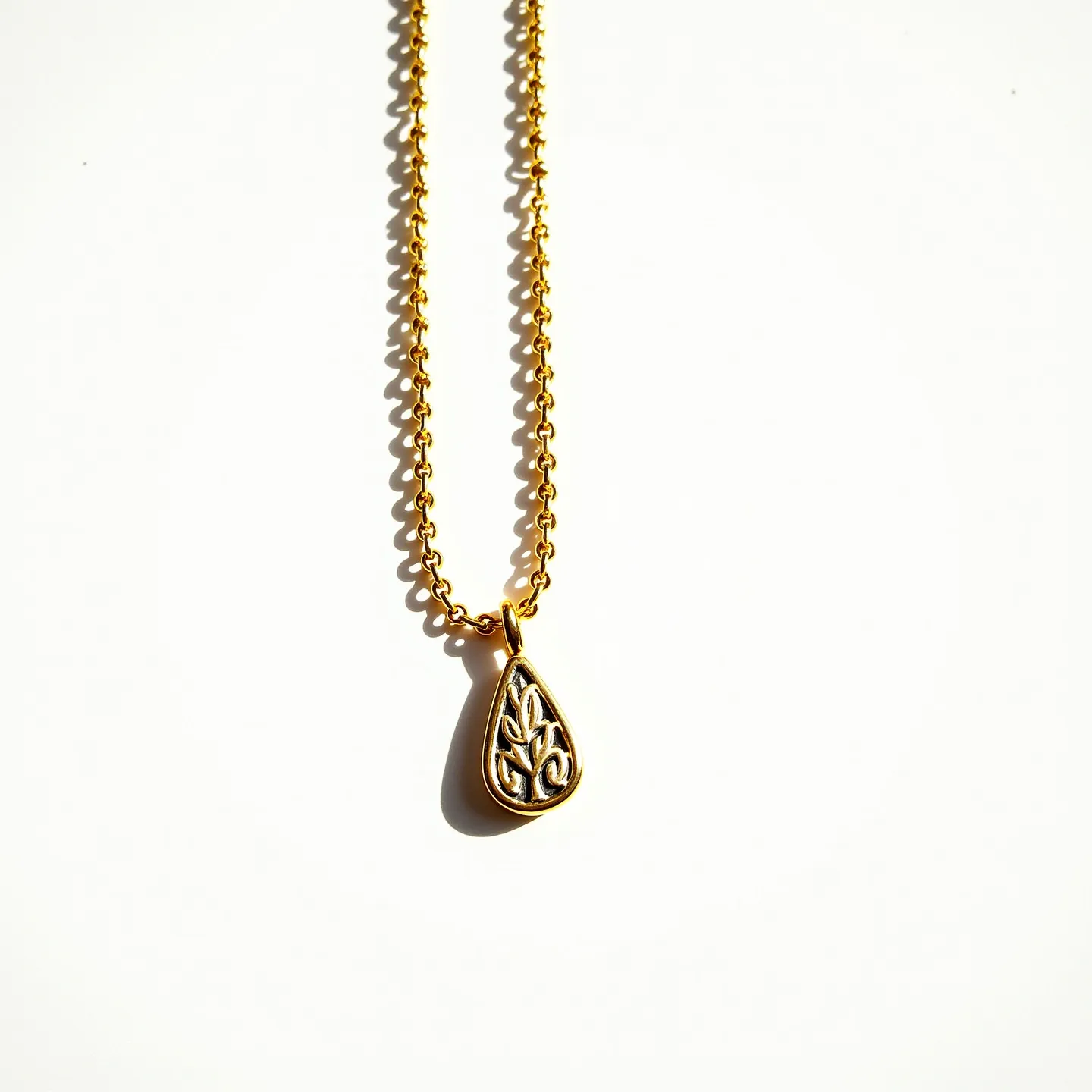 This drop necklace features a gold-toned chain with a teardrop-shaped pendant. The pendant showcases an intricate design, possibly intricate filigree work, within its frame. The chain links appear to be uniformly oval-shaped, giving it a classic and consistent look. The pendant is attached to the chain with a simple, elegant bail that matches the gold tone of the chain and pendant. There is no visible clasp in this view, suggesting it may be located at the back or side. The overall design is sleek and modern, with a hint of timeless elegance.