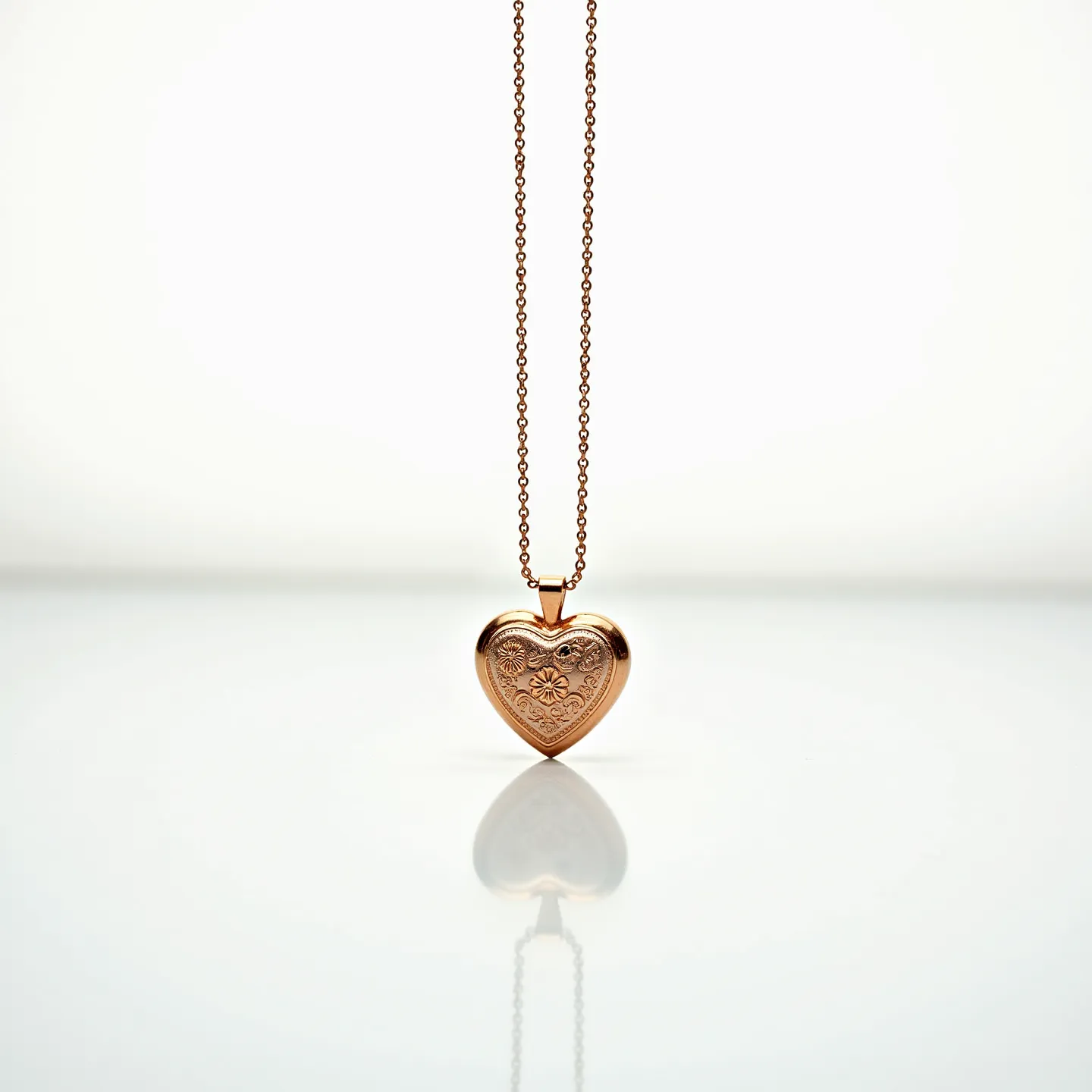 This engraved heart necklace features a beautifully detailed heart-shaped pendant crafted from a warm, metallic material, possibly gold or gold-toned. The pendant showcases intricate floral engravings that add a touch of elegance and craftsmanship. While it does not feature any visible gems or stones, the design's charm lies in its simple yet sophisticated engravings. The heart pendant is attached to a delicate chain, which appears to be made of the same material, giving a unified and harmonious look. The connection between the pendant and the chain seems secure, with a small bail, allowing for smooth movement.