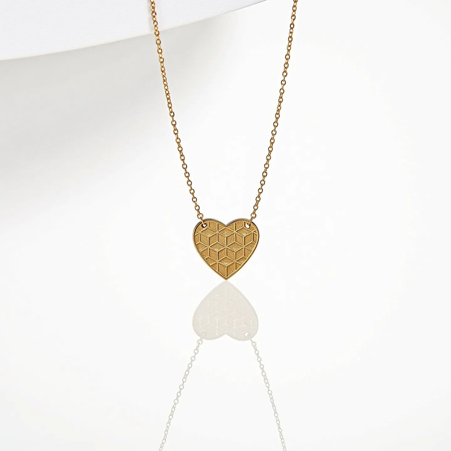 This engraved heart necklace features a gold-toned metal pendant intricately designed with a geometric pattern. The pendant is suspended on a delicate matching chain, adding to its elegant appearance. The heart pendant's surface is engraved with a series of repeating cubic shapes that create an eye-catching texture. It is attached to the chain with simple loops, which allow it to hang gracefully. The chain likely includes a standard clasp for securing around the neck, ensuring ease of wear.