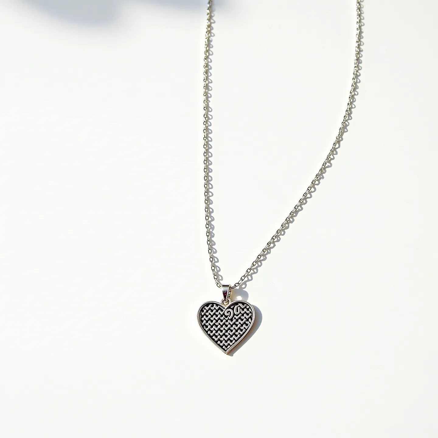 This engraved heart necklace features a finely crafted heart-shaped pendant with an intricate engraved pattern on its surface. The pendant is likely made from a polished metal, possibly silver or stainless steel, giving it a shiny, reflective appearance. There are no visible gems embedded in the design. The pendant is attached to a delicate chain, also crafted from a similar polished metal, that complements the pendant's elegant look. The chain is secured with a simple yet functional clasp, ensuring easy wear and removal.