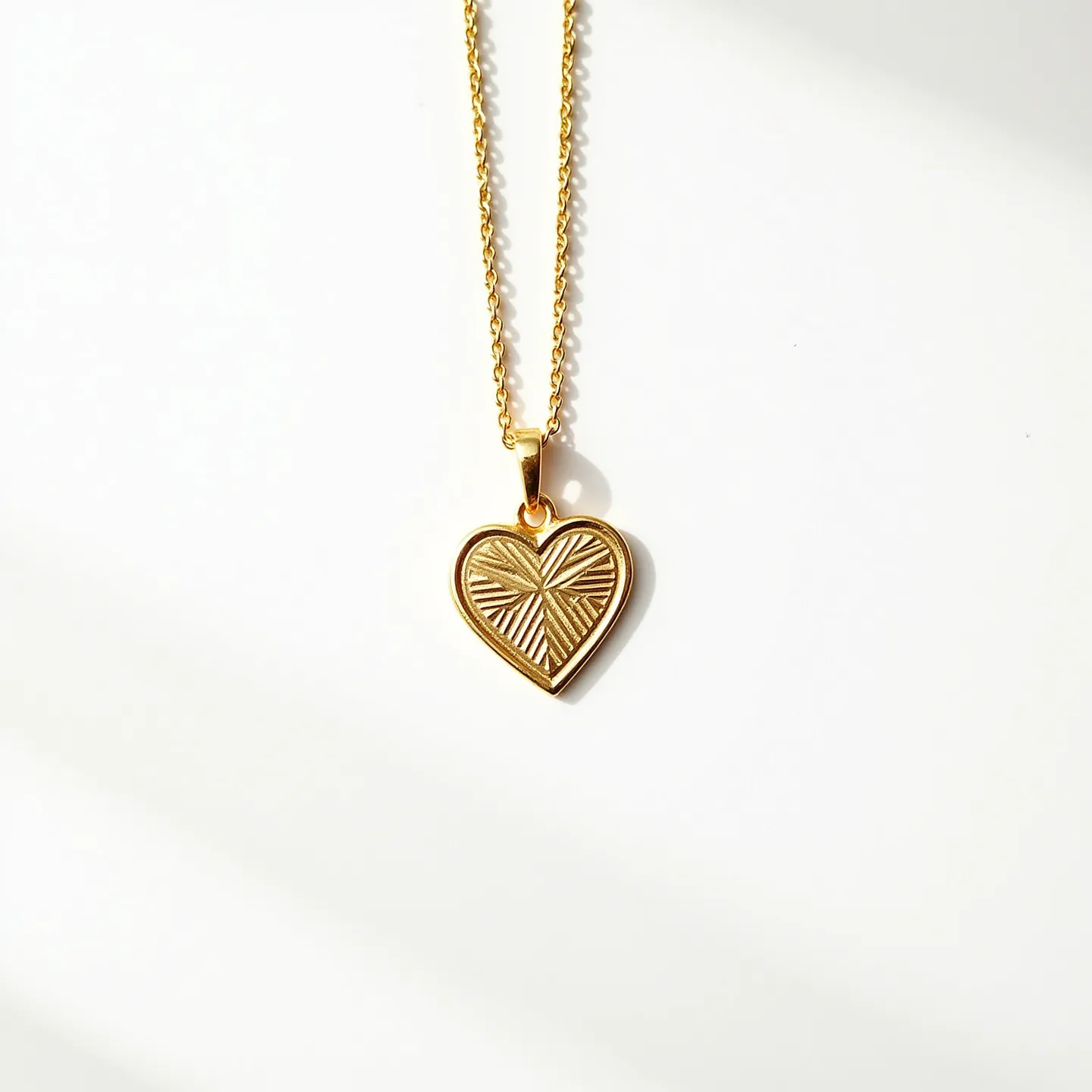 This engraved heart necklace features a charming heart-shaped pendant crafted from what appears to be gold or a gold-toned metal. The pendant is adorned with a radiating engraved pattern, adding texture and visual interest. It hangs from a delicate chain, also gold in color, which complements the pendant's elegant design. The necklace is secured with a traditional clasp, ensuring a secure fit while being worn. The simplicity and elegance make it a versatile accessory for various occasions.