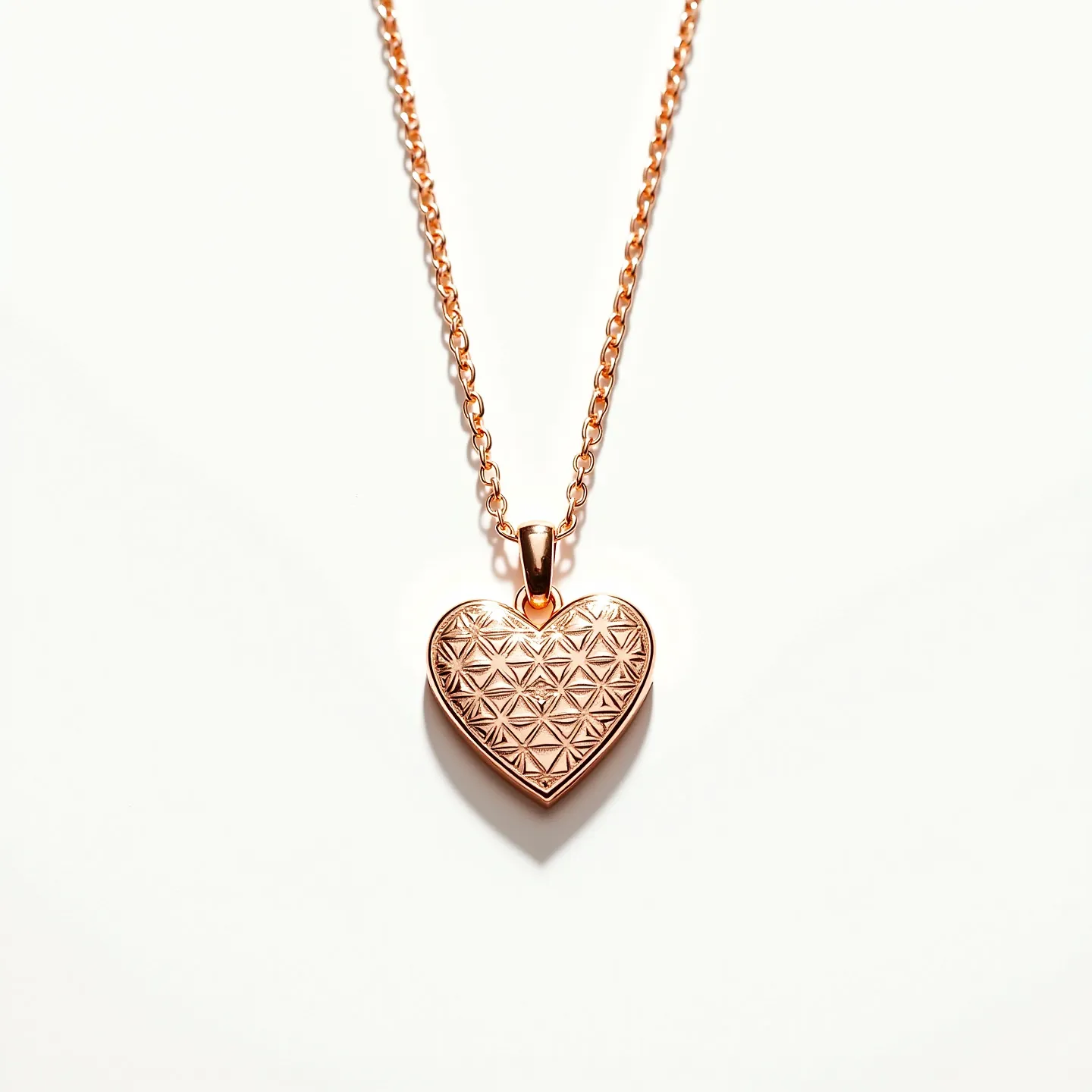 This engraved heart necklace features a chain and heart pendant both crafted from a warm, rose gold-tone metal. The pendant showcases an intricate geometric pattern, adding texture and visual interest to its surface. The heart is suspended from a matching bail, which seamlessly connects it to the delicate chain. This necklace does not include any gemstones, allowing the detailed engraving to stand out as the main feature. The chain is likely secured with a classic clasp, ensuring both functionality and elegance.