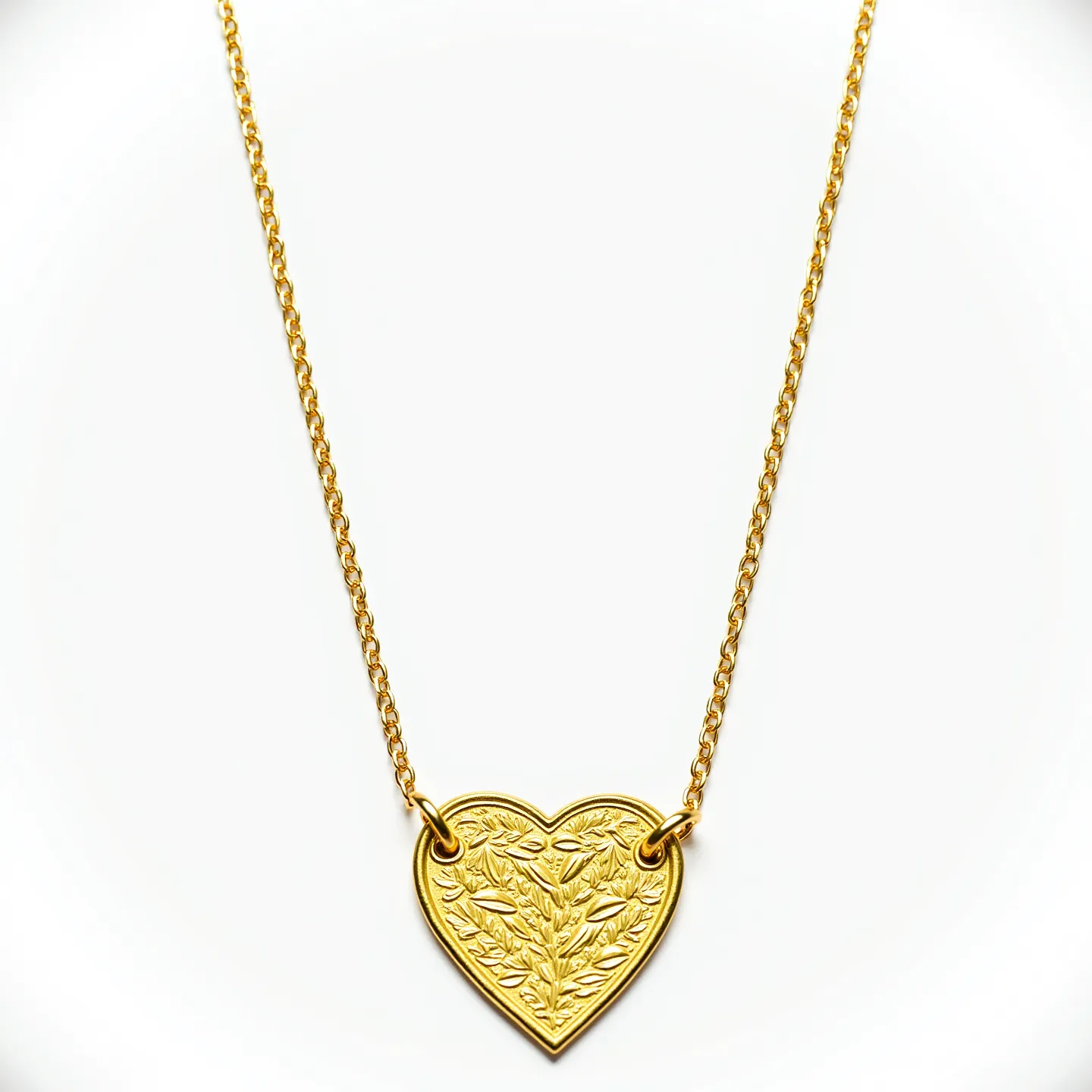 This engraved necklace features a heart-shaped pendant crafted from gold-toned metal, elegantly suspended from a matching chain. The heart pendant is intricately designed with a floral motif, showcasing finely detailed leaves and stems etched across its surface. The pendant is attached to the chain via two small rings, enhancing the overall aesthetic with a balanced and symmetrical appearance. The chain appears to be a delicate cable style, known for its classic and versatile appeal. The clasp, although not visible, is likely to be a standard spring ring or lobster clasp, commonly used for secure and easy fastening in necklaces of this type.