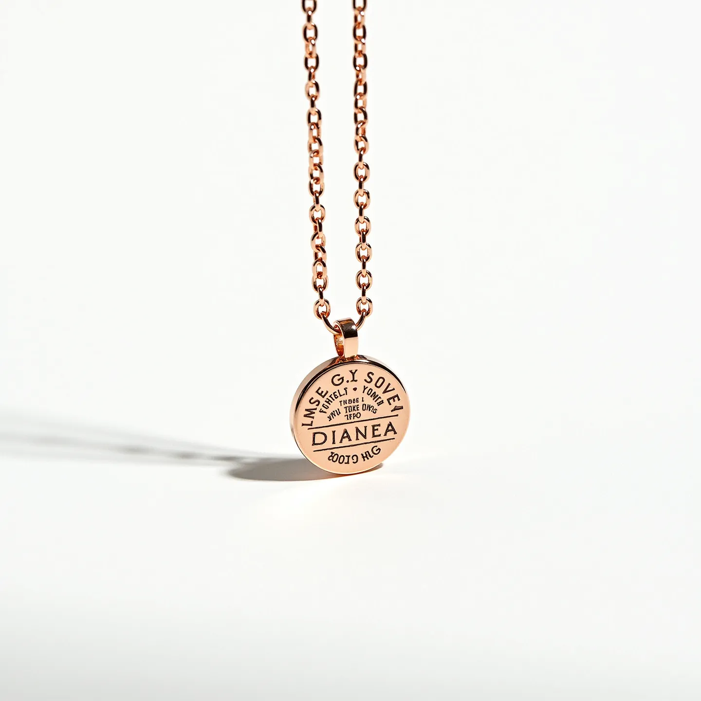 This engraved necklace features a round pendant made of a metal that resembles rose gold, inscribed with various text elements that add a personalized touch. The chain is composed of rounded links, matching the pendant's rose gold hue, providing a cohesive, polished look. The pendant relies on a classic bale-style attachment, seamlessly connecting to the chain, which likely fastens with a standard clasp for ease of wear. The minimalist design and warm metallic tones combine to create an elegant piece that is both trendy and enduringly stylish.