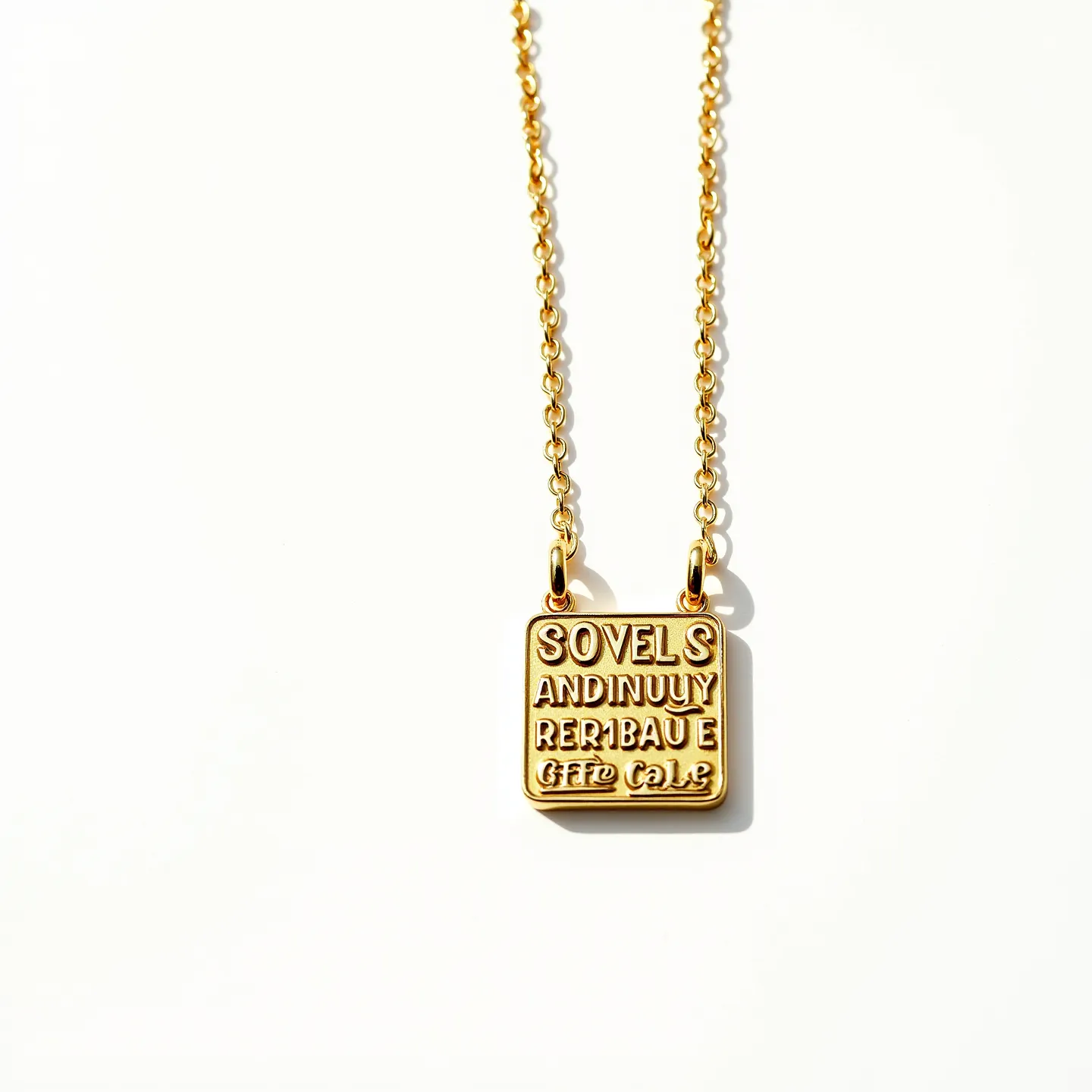 This engraved necklace features a square pendant with embossed lettering, crafted from what appears to be a gold-toned metal. The pendant is suspended from a delicate chain the same gold hue, suggesting a cohesive design. The chain is connected to the pendant through two small loops, which are securely attached to the top corners of the square. The necklace does not feature any gemstones, focusing instead on the metallic finish and the unique text engraving on the surface. The chain's links are small and uniform, adding to the understated elegance of the piece.