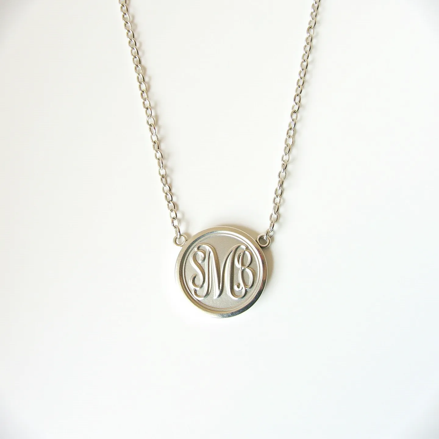 This engraved necklace features a sleek, circular pendant crafted from a metallic material, possibly silver or stainless steel, showcasing an engraved monogram. The pendant is smoothly integrated into a matching chain composed of interlocking links, which enhances the overall elegance of the piece. The chain appears to use a standard clasp mechanism for easy attachment, ensuring both security and style. The craftsmanship highlights a minimalist design with a polished finish that accentuates the monogram's intricacy.