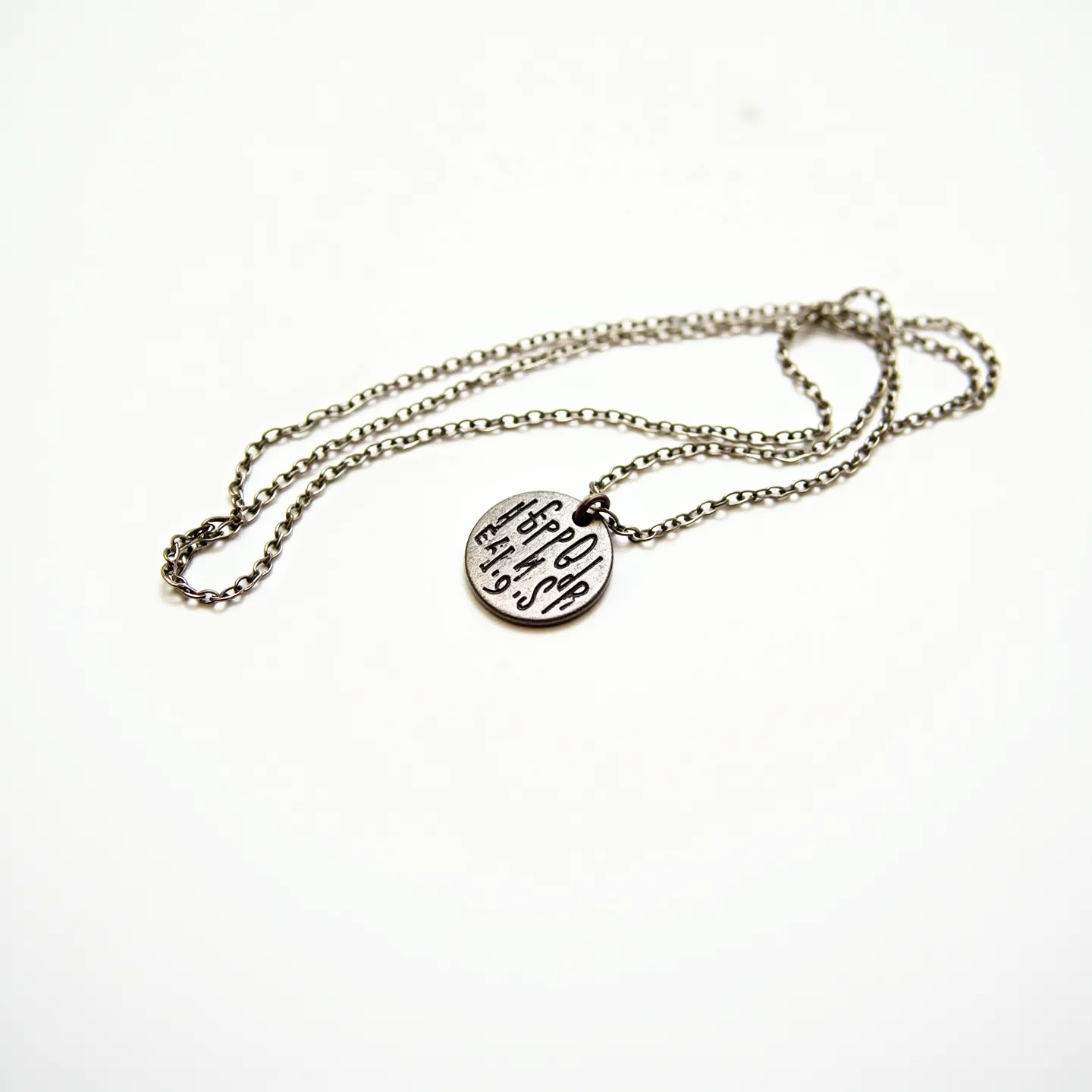 This engraved necklace features a round pendant with intricate engraved markings on its surface. The pendant is attached to a delicate chain made of a likely metallic material, providing a sleek and understated appearance. The design of the chain complements the pendant, both in texture and style. No gemstones are present in the necklace, allowing the engraved details to be the focal point. The chain is equipped with a standard clasp, offering a secure closure.